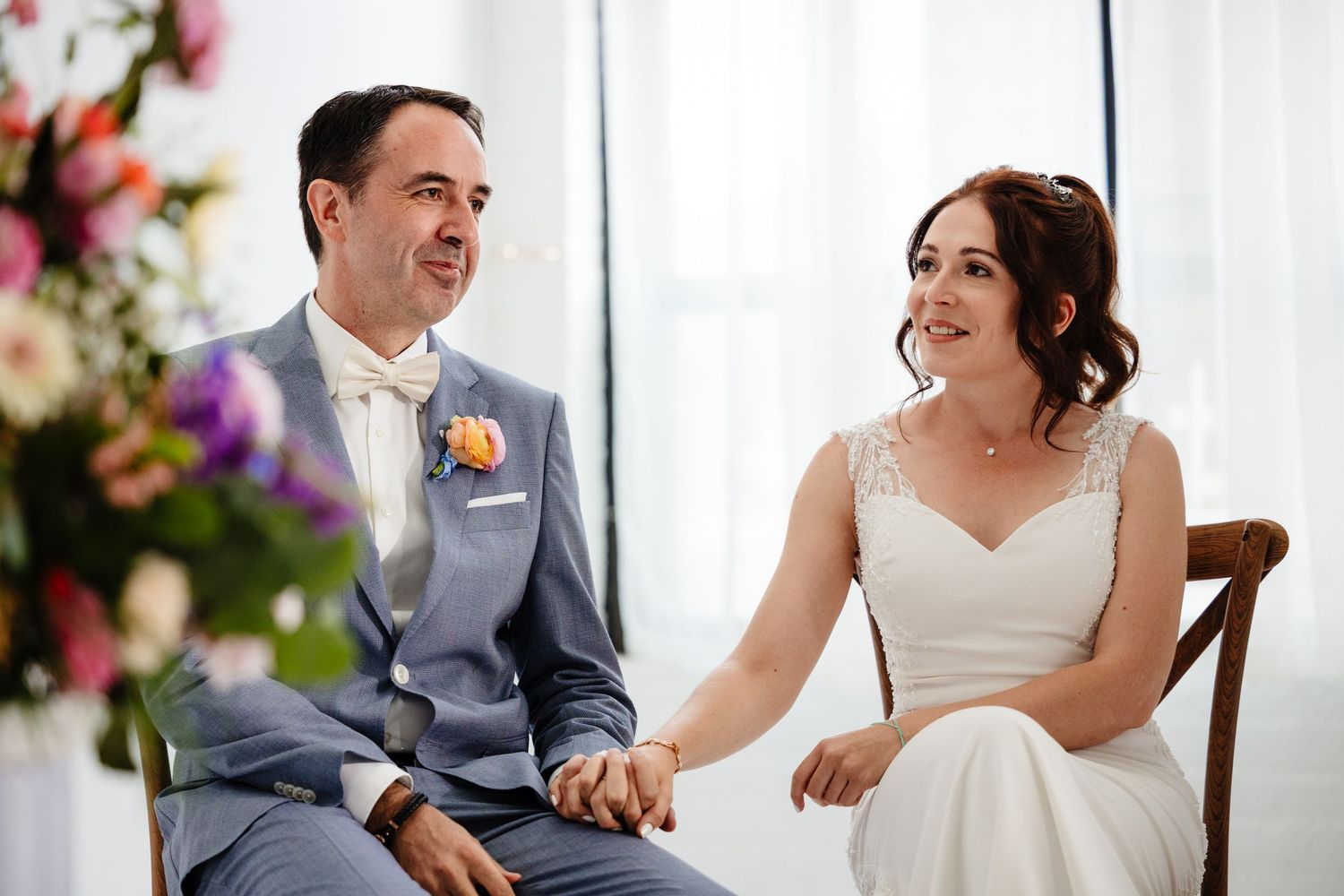 Couple shares a candid moment during their wedding photoshoot in a bright, window-lit venue.