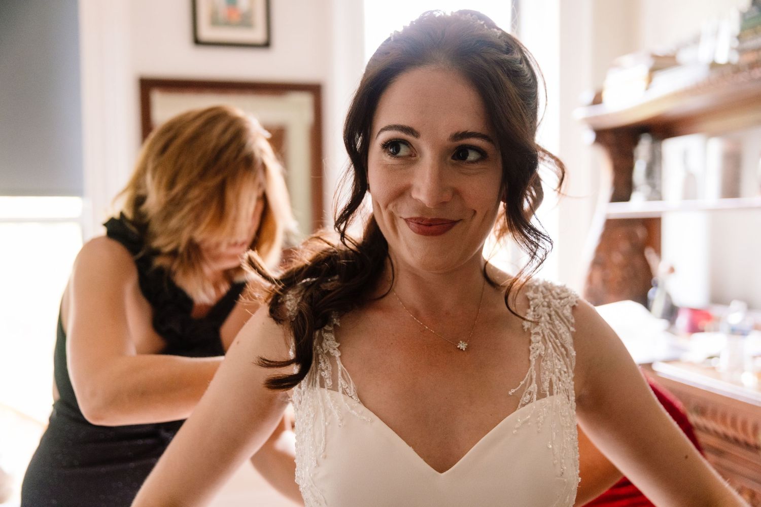 A close-up shot of someone getting ready in a white wedding dress with delicate details.