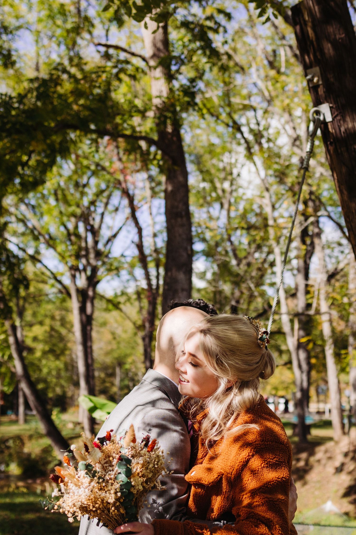 A couple embraces in a autumn forest setting holding a dried flower bouquet.