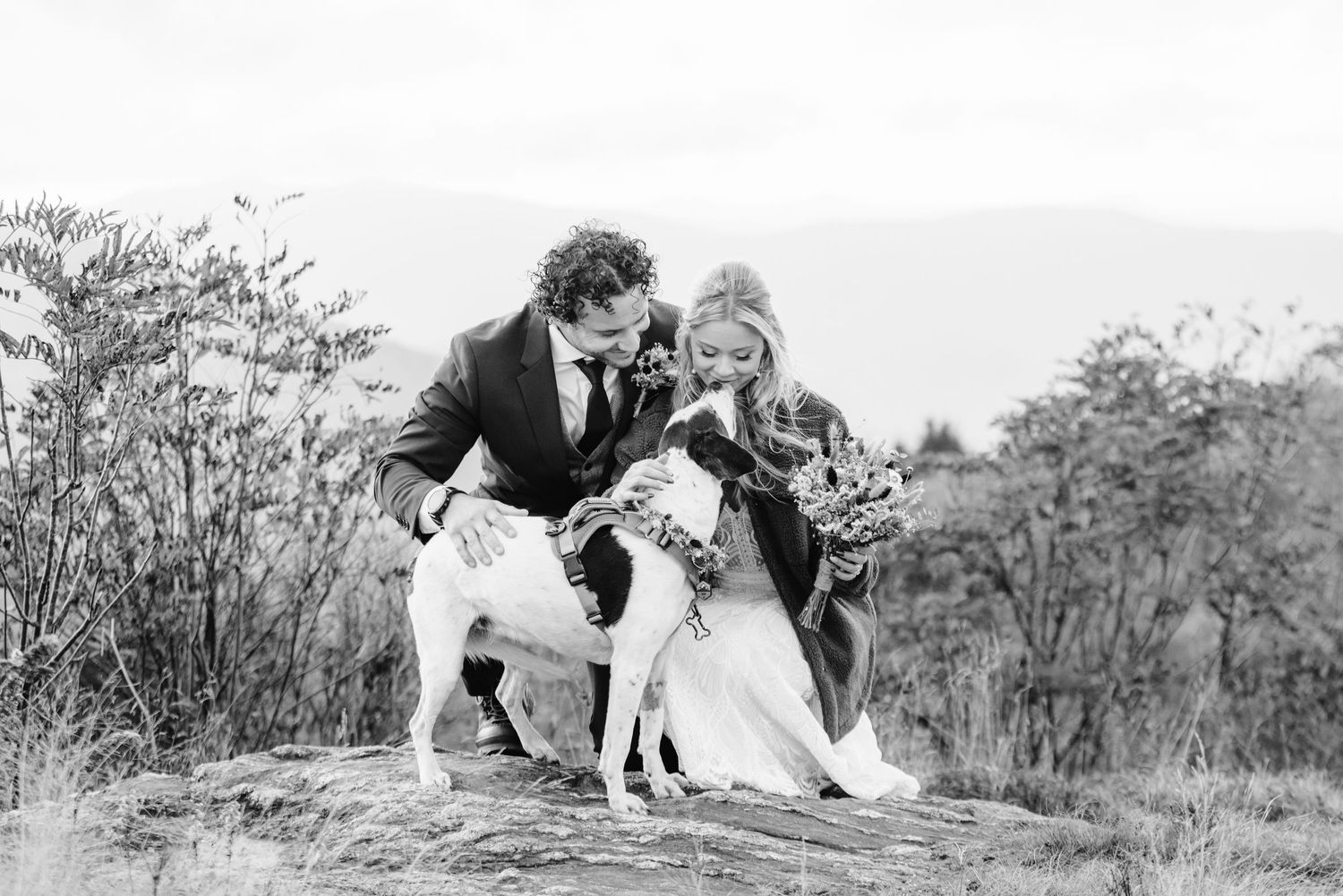 Black and white photograph of couple with their dog on a hillside.