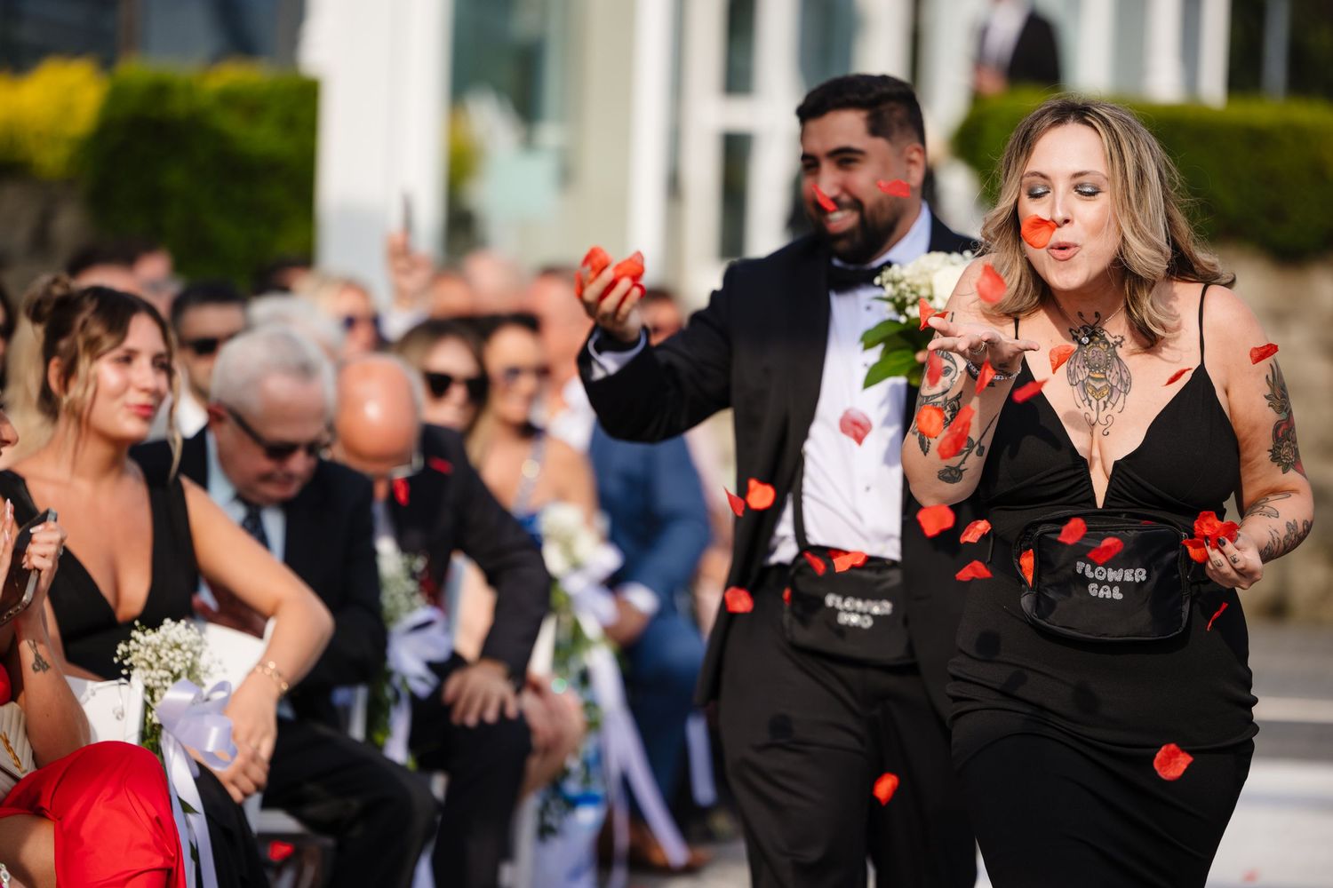 Wedding guests throw red rose petals during an outdoor celebration.