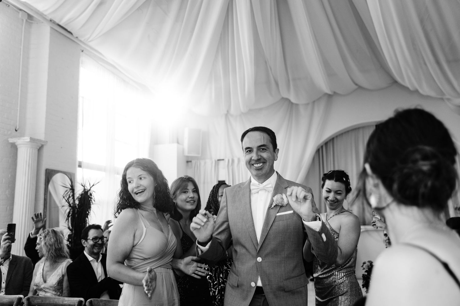 Wedding celebration crowd raises their hands in celebration during a festive reception moment.