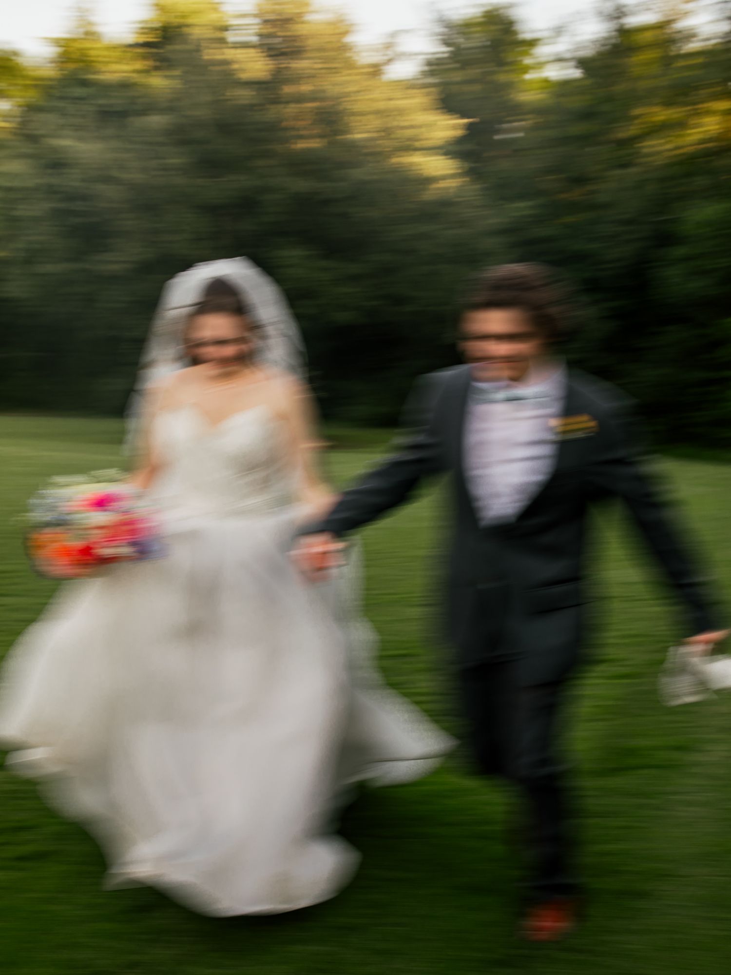 Bride and groom run with each other in a field. She is holding a bouquet and he is holding her shoes.