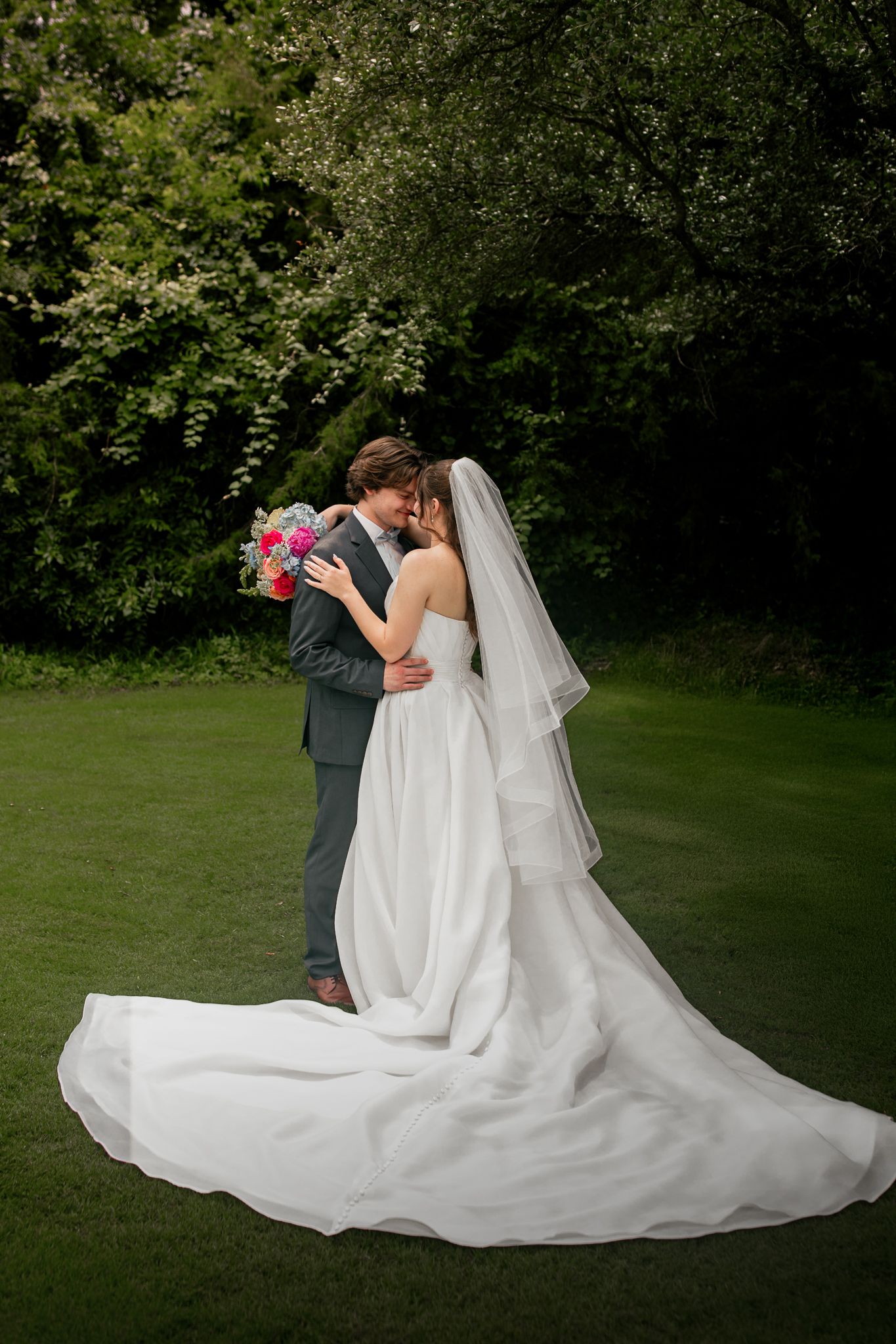 Bride and groom stand with each other in a field in Waco, Texas. They are holding each other and smiling softly.