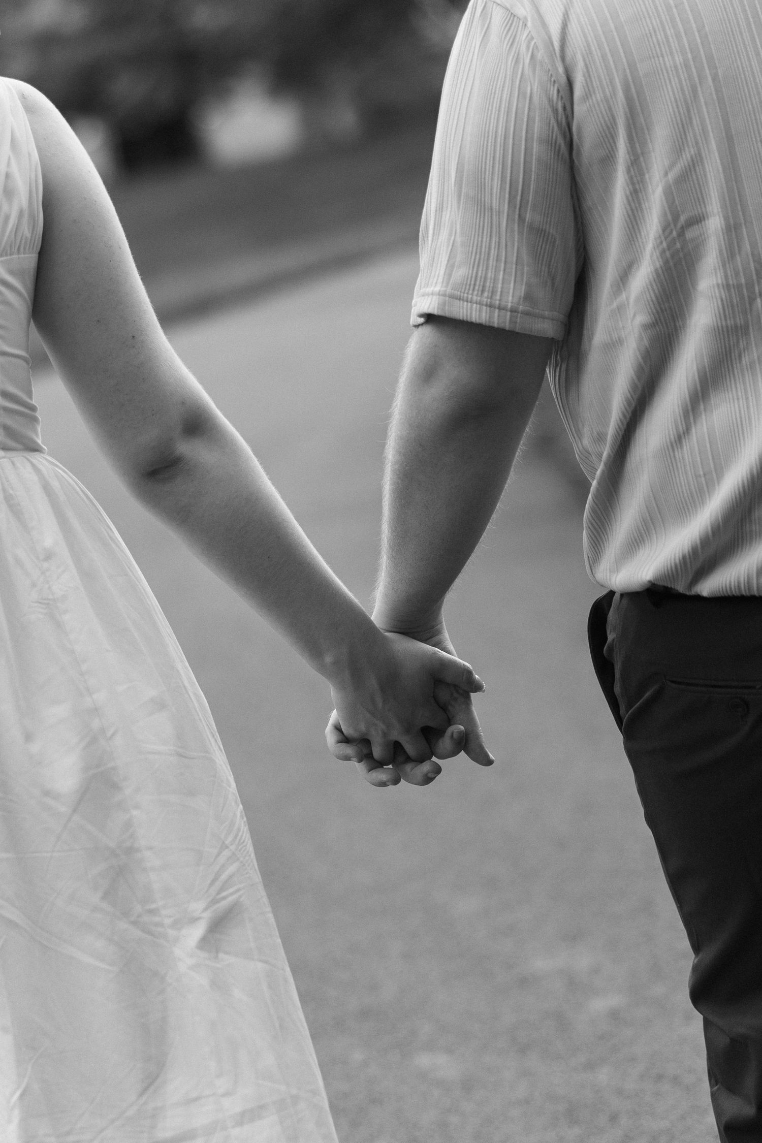 Black and white close-up of a couple holding hands while walking, she in a white dress.