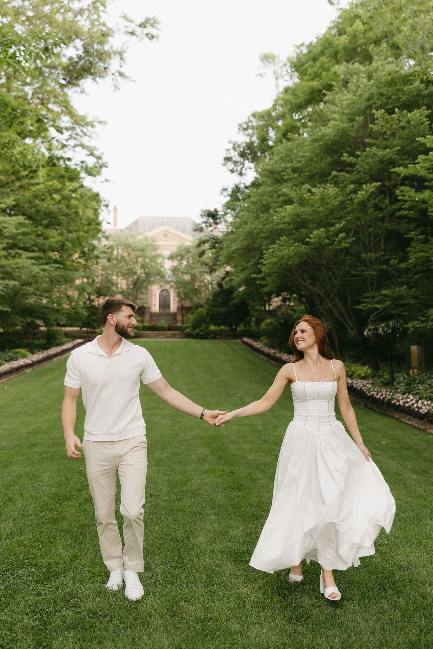 Smiling couple holds hands while walking through a manicured green garden landscape.