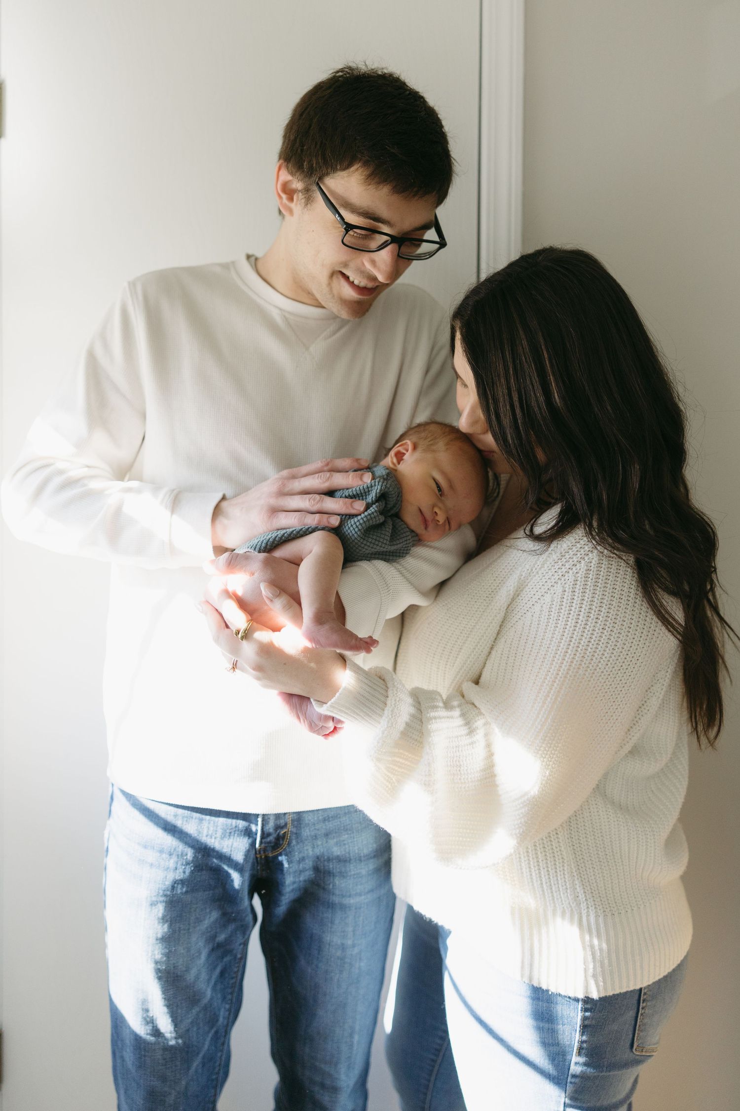 New parents in casual attire lovingly gazing at their sleeping newborn baby together.