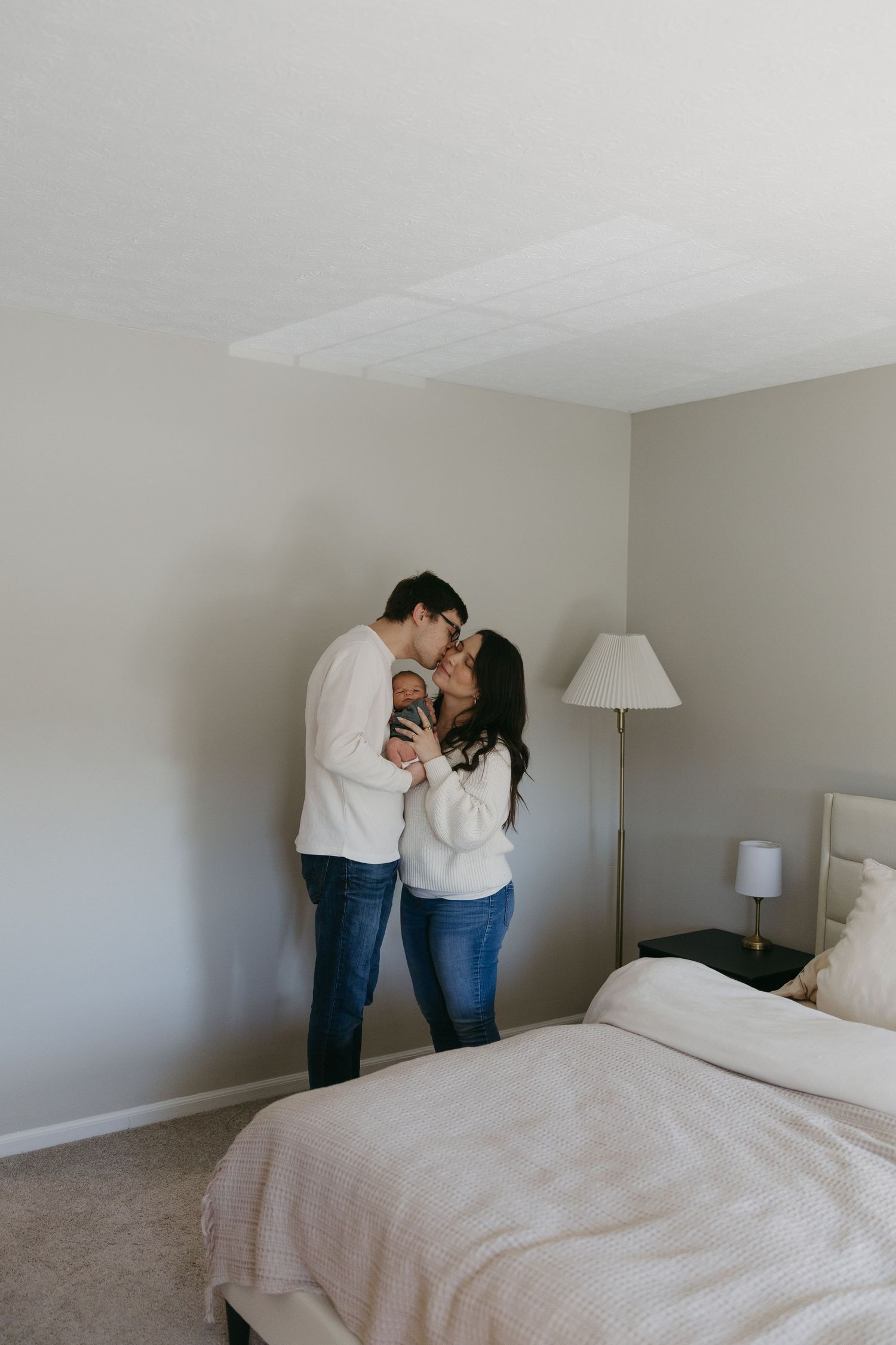 Couple sharing a tender kiss in a cozy bedroom during an intimate engagement photo session.