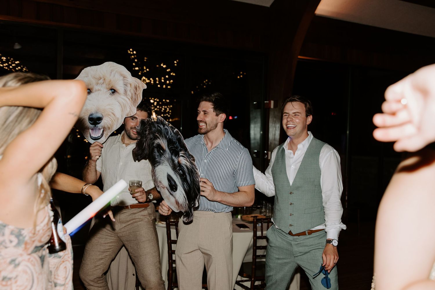 People laughing at a party with someone wearing a large dog mascot head costume at an indoor event.