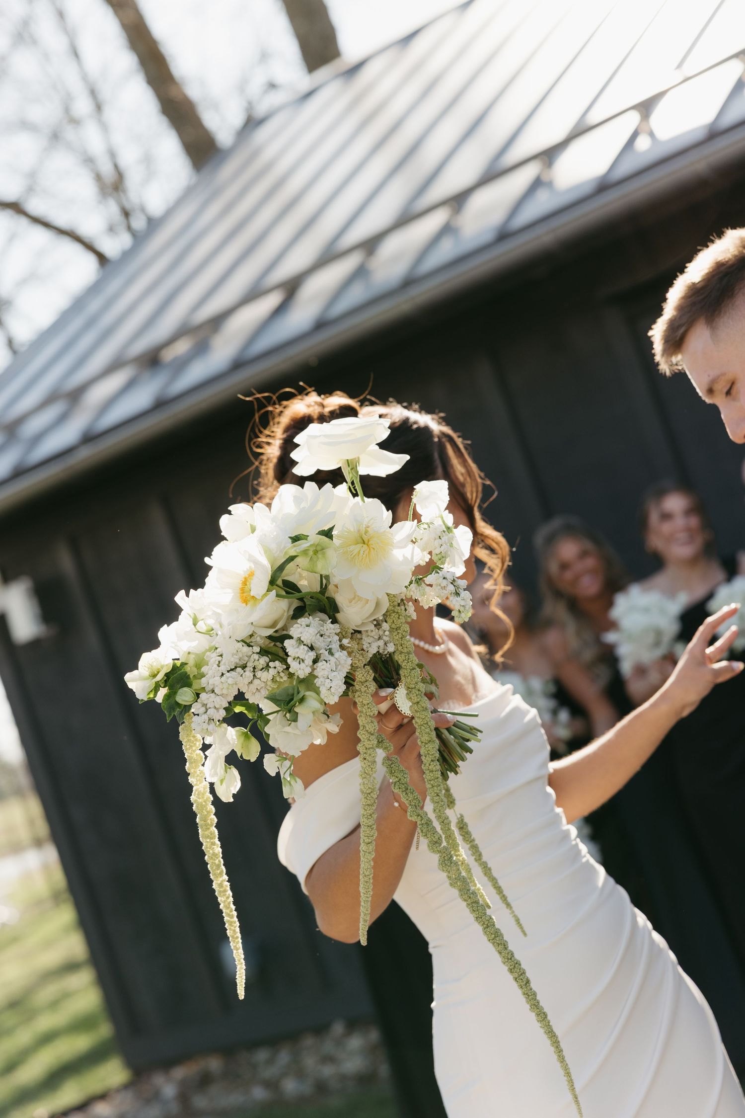 Bride holds a lush cascading white floral bouquet with greenery while dancing outdoors.