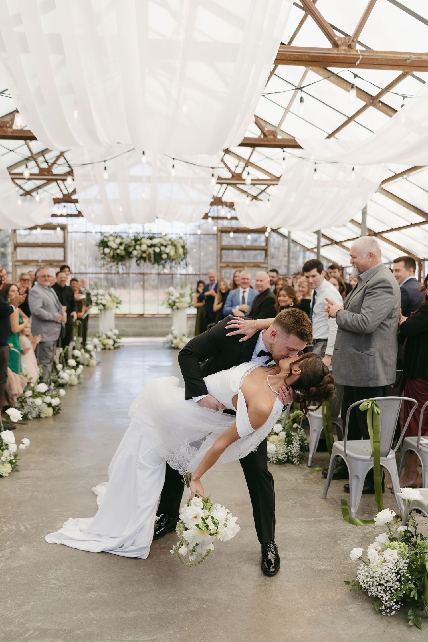 Groom dips bride for a romantic kiss at the end of the aisle in a stunning greenhouse wedding ceremony.