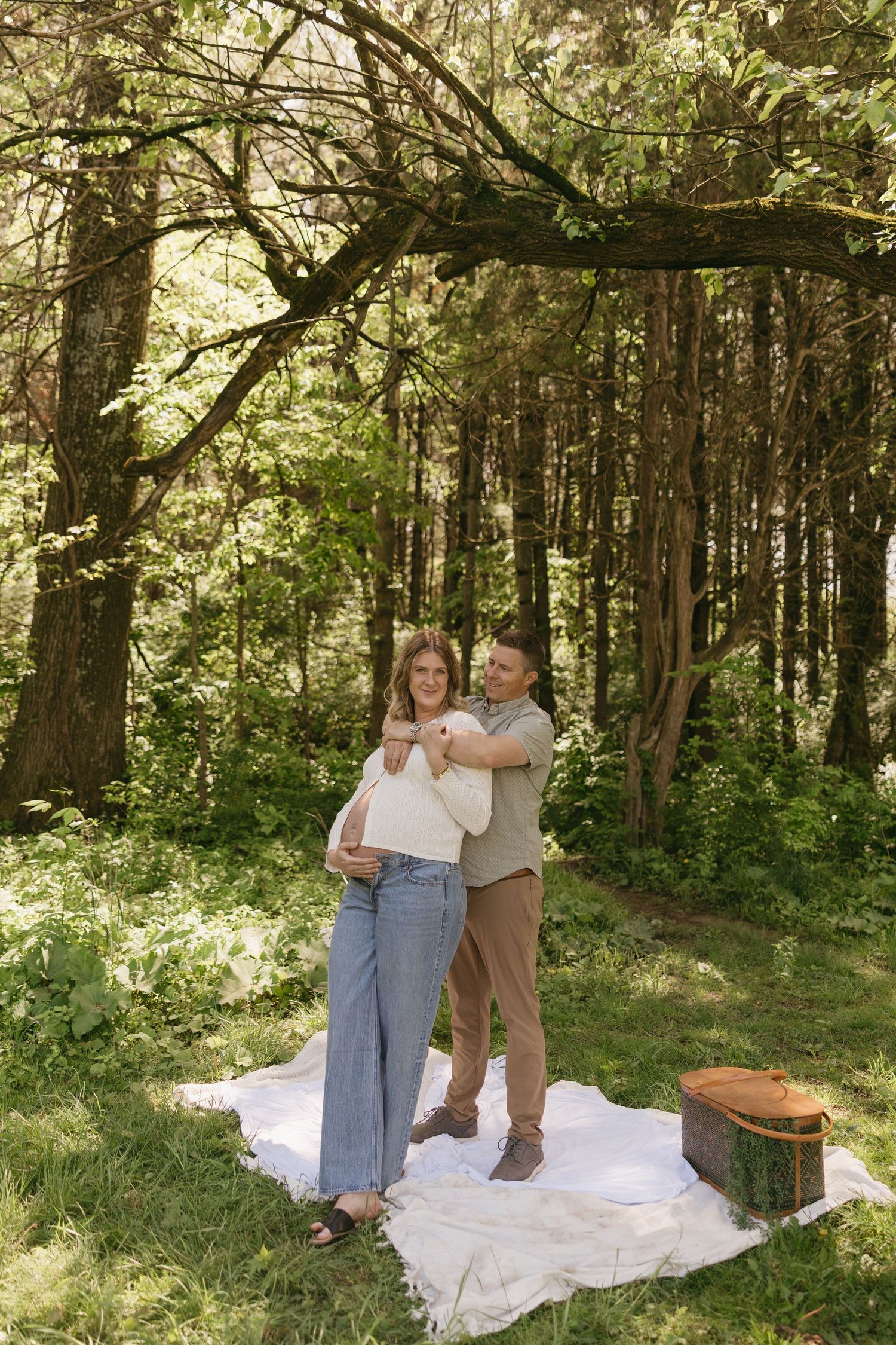 Couple embracing on a white blanket during a picnic in a lush green forest.