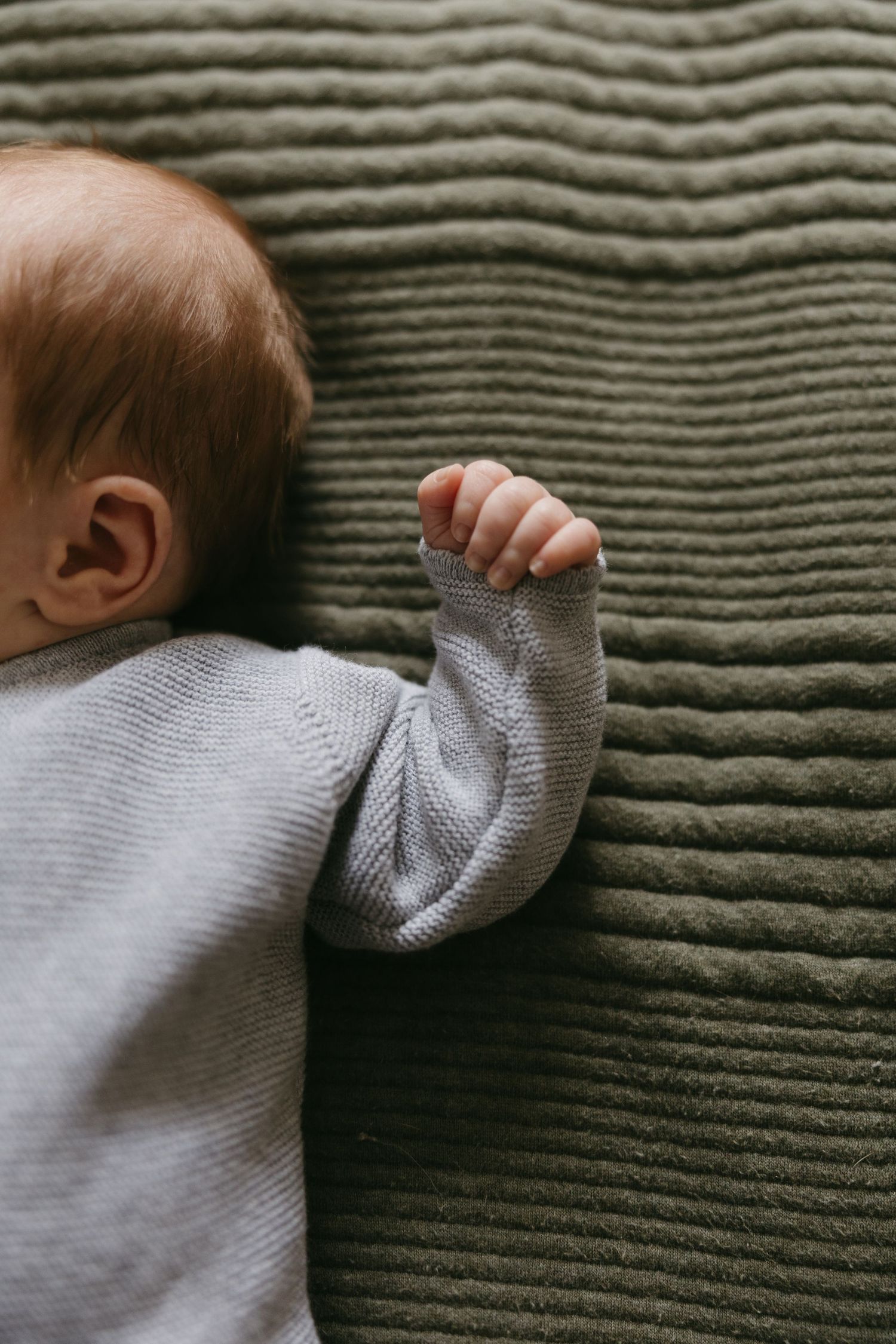 Close-up of a newborn baby in a gray knit onesie lying on a green textured blanket.