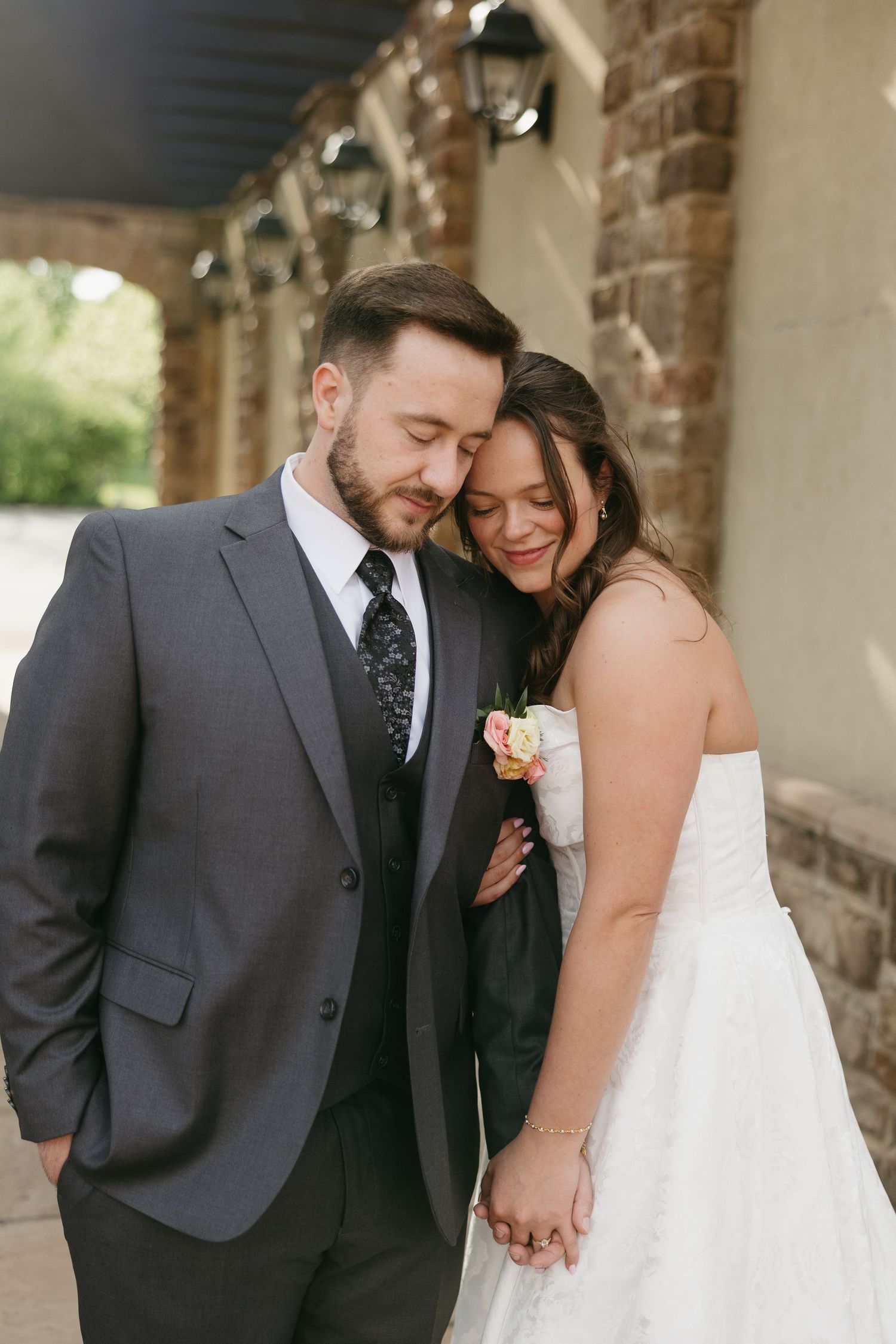 Bride and groom share a tender moment holding hands outside a brick building on their wedding day.