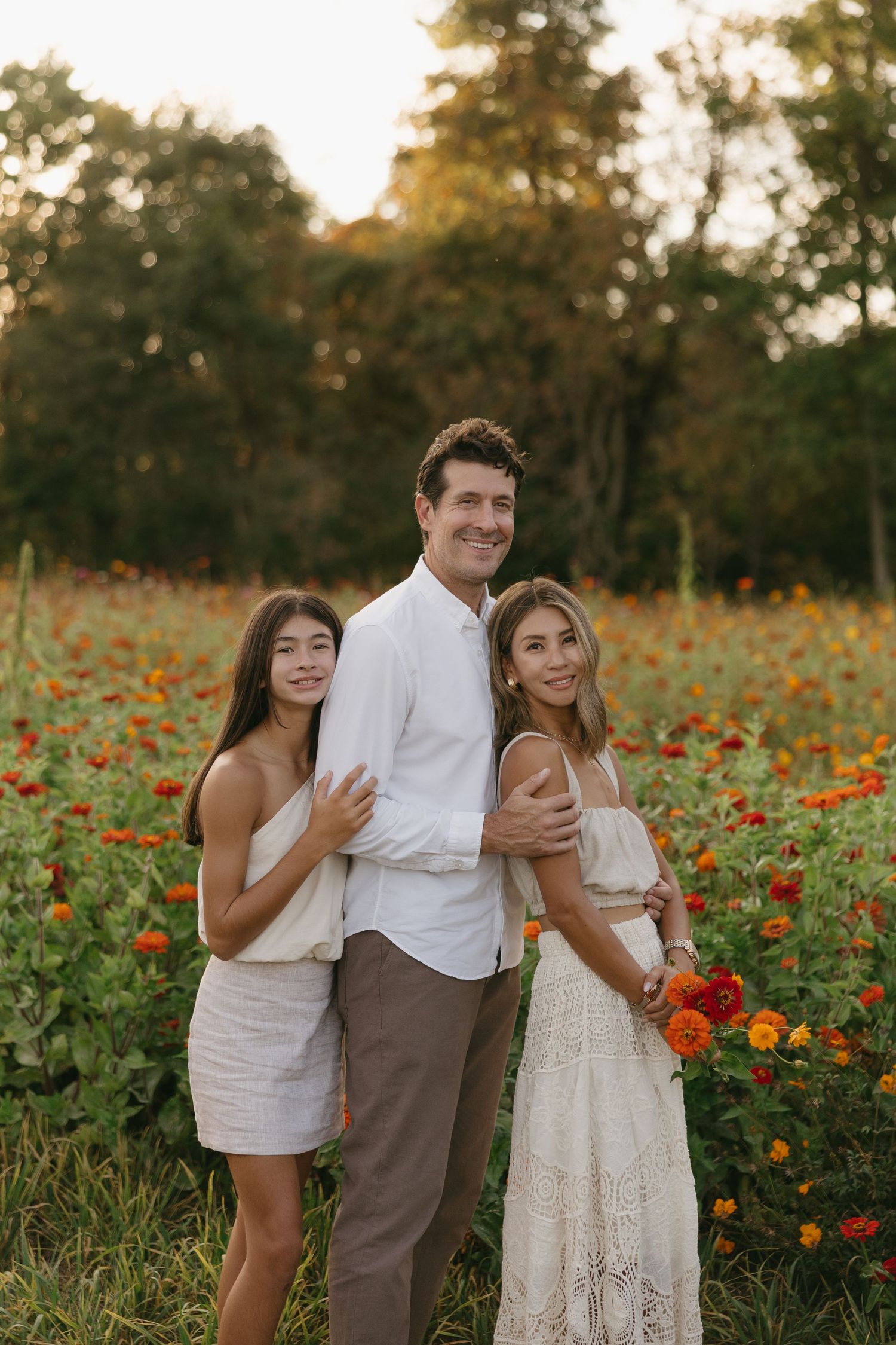Family of three posing together in a vibrant zinnia flower field at golden hour.