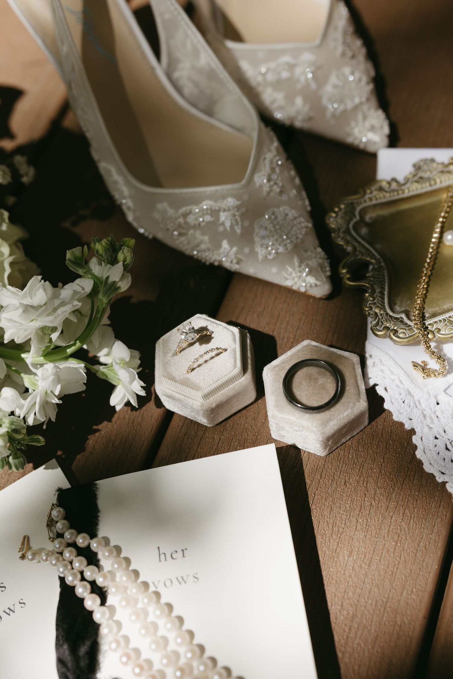 Elegant wedding flat lay with bridal heels, ring boxes, pearl necklace, and vow booklet.