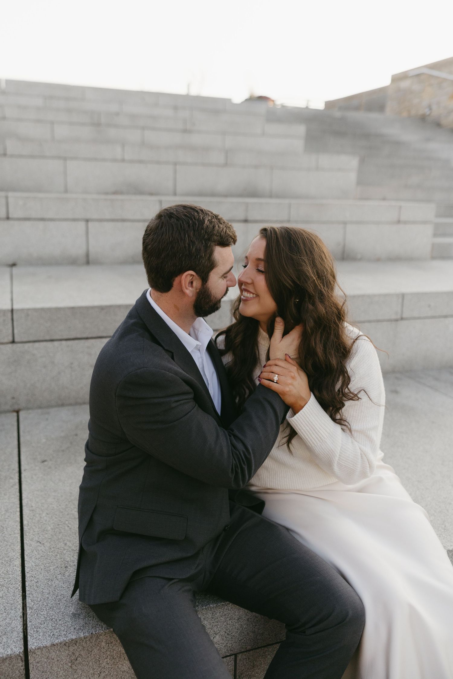 Couple sharing an intimate almost-kiss moment while seated on marble steps outdoors.