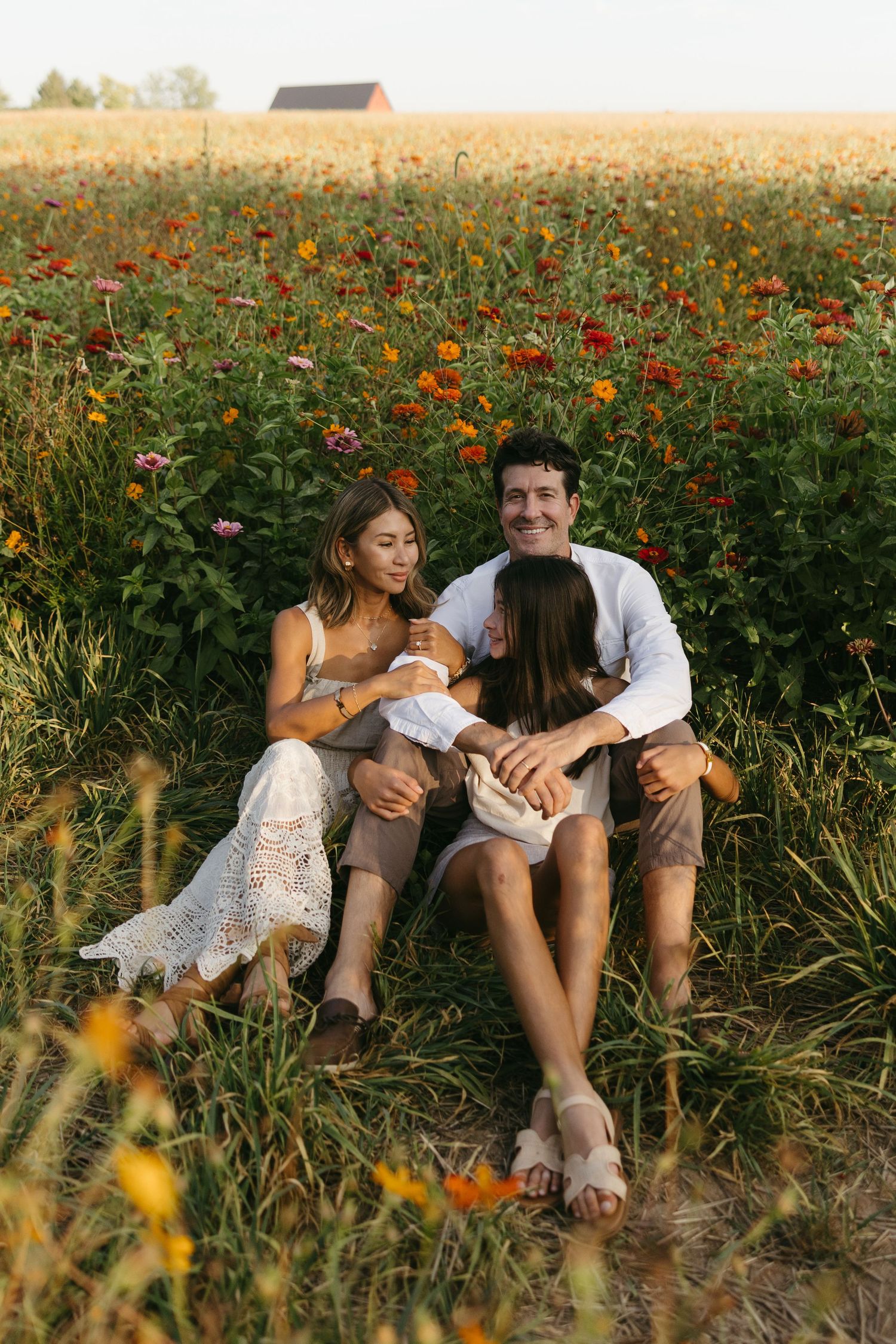 Happy family of three sitting together in a vibrant colorful flower field at sunset.