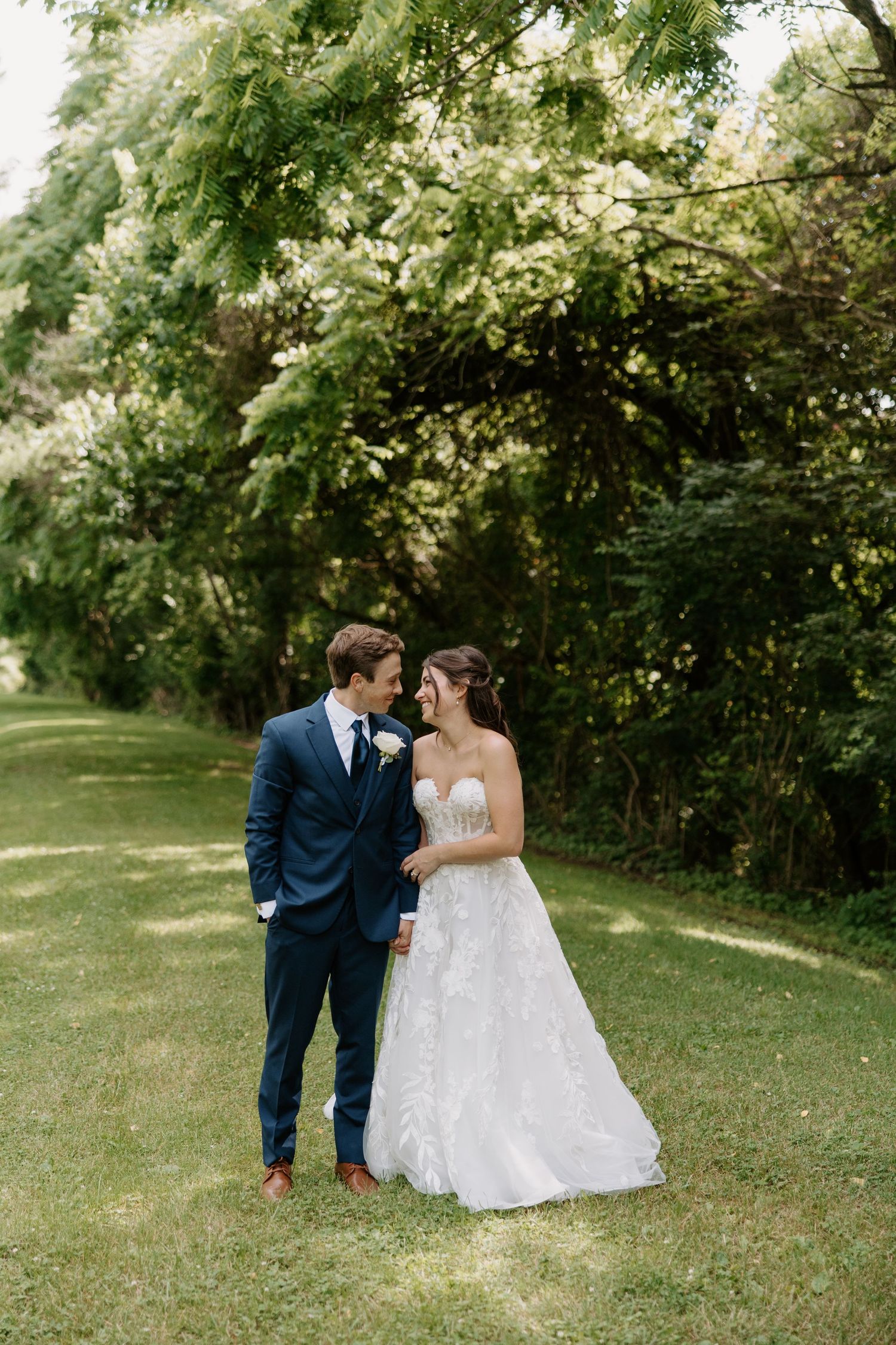 Bride and groom share a romantic moment on lush green lawn surrounded by blooming trees on their wedding day.
