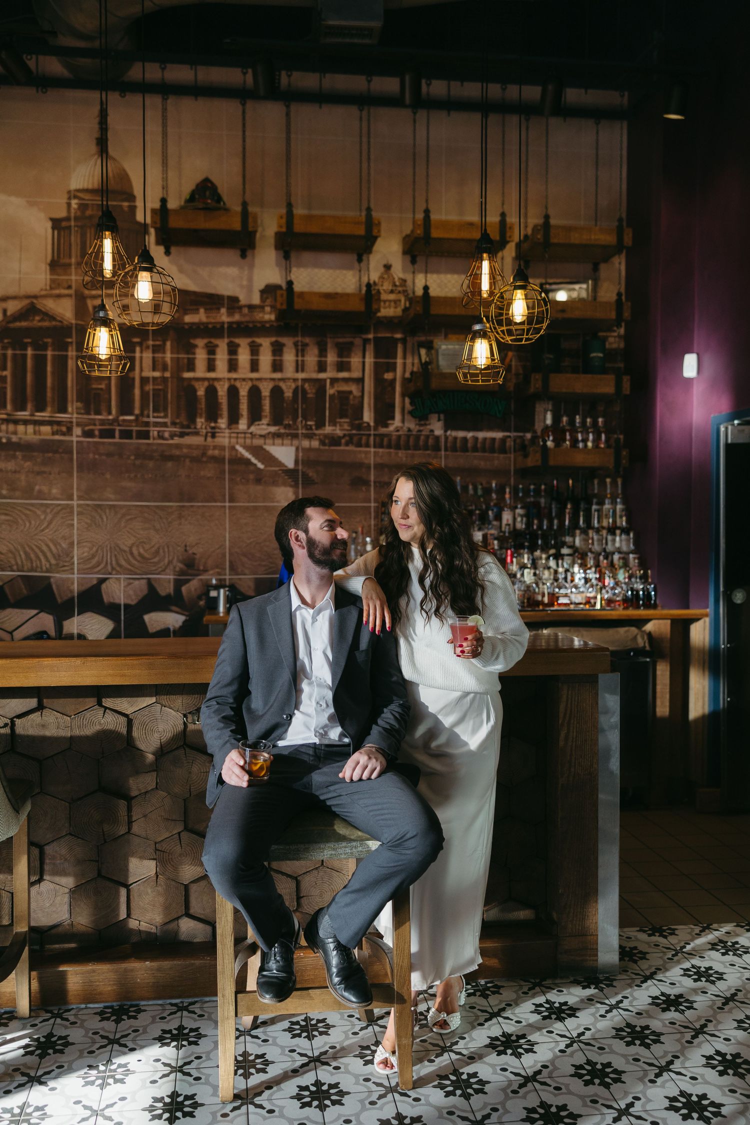 Stylish couple relaxing at a moody bar with Edison bulb lighting, sharing drinks together.