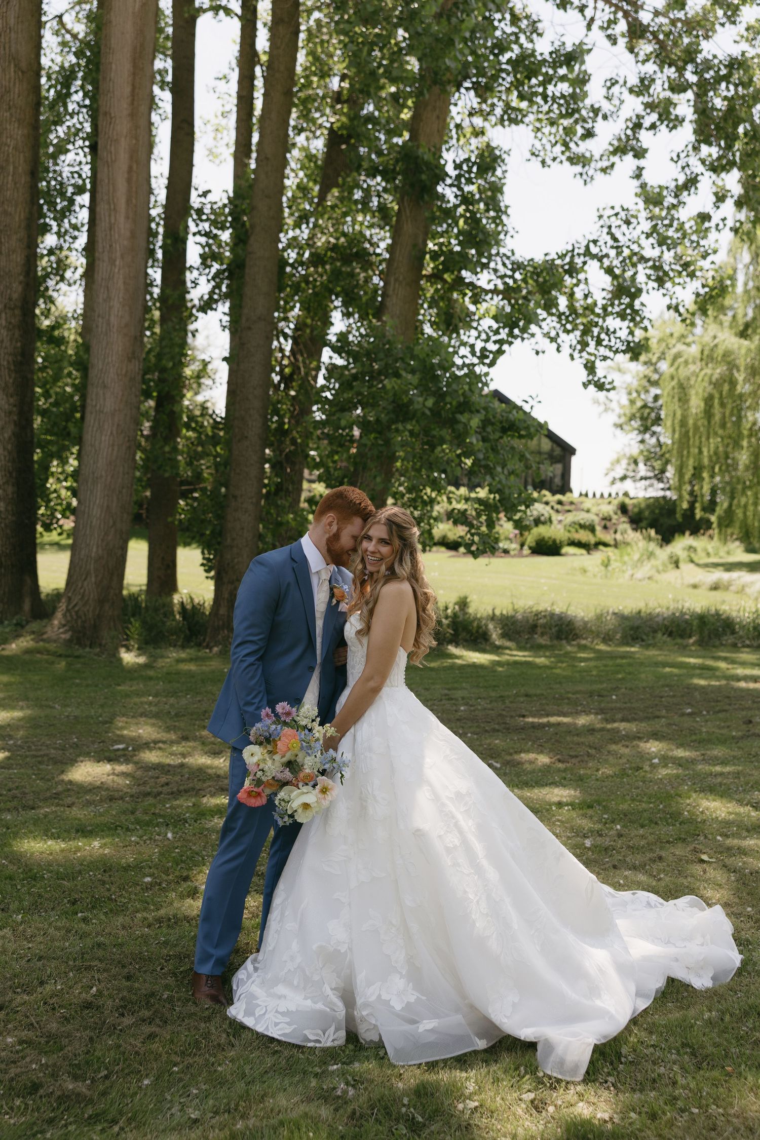 Bride and groom embracing outdoors in lush garden, bride holding colorful bouquet in white gown.