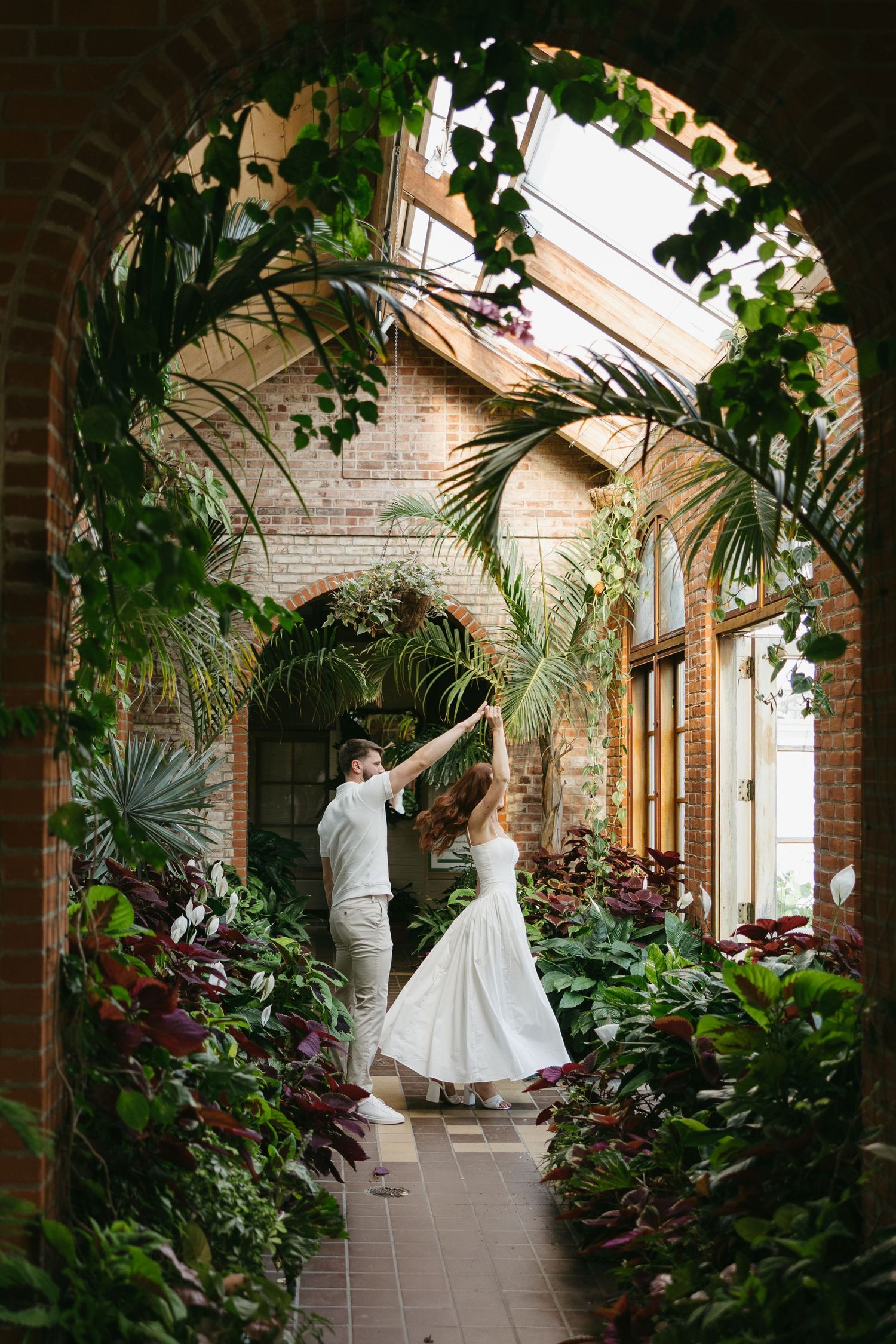 Bride and groom dancing under a lush tropical archway inside a stunning botanical conservatory.