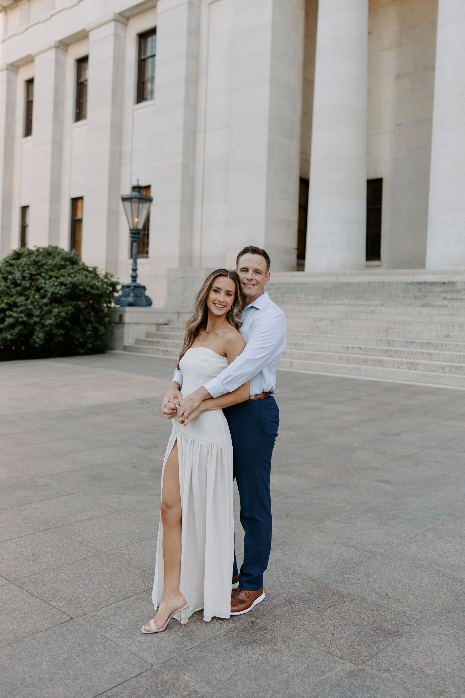 Couple embracing and smiling in front of a grand neoclassical building during an engagement photo session.