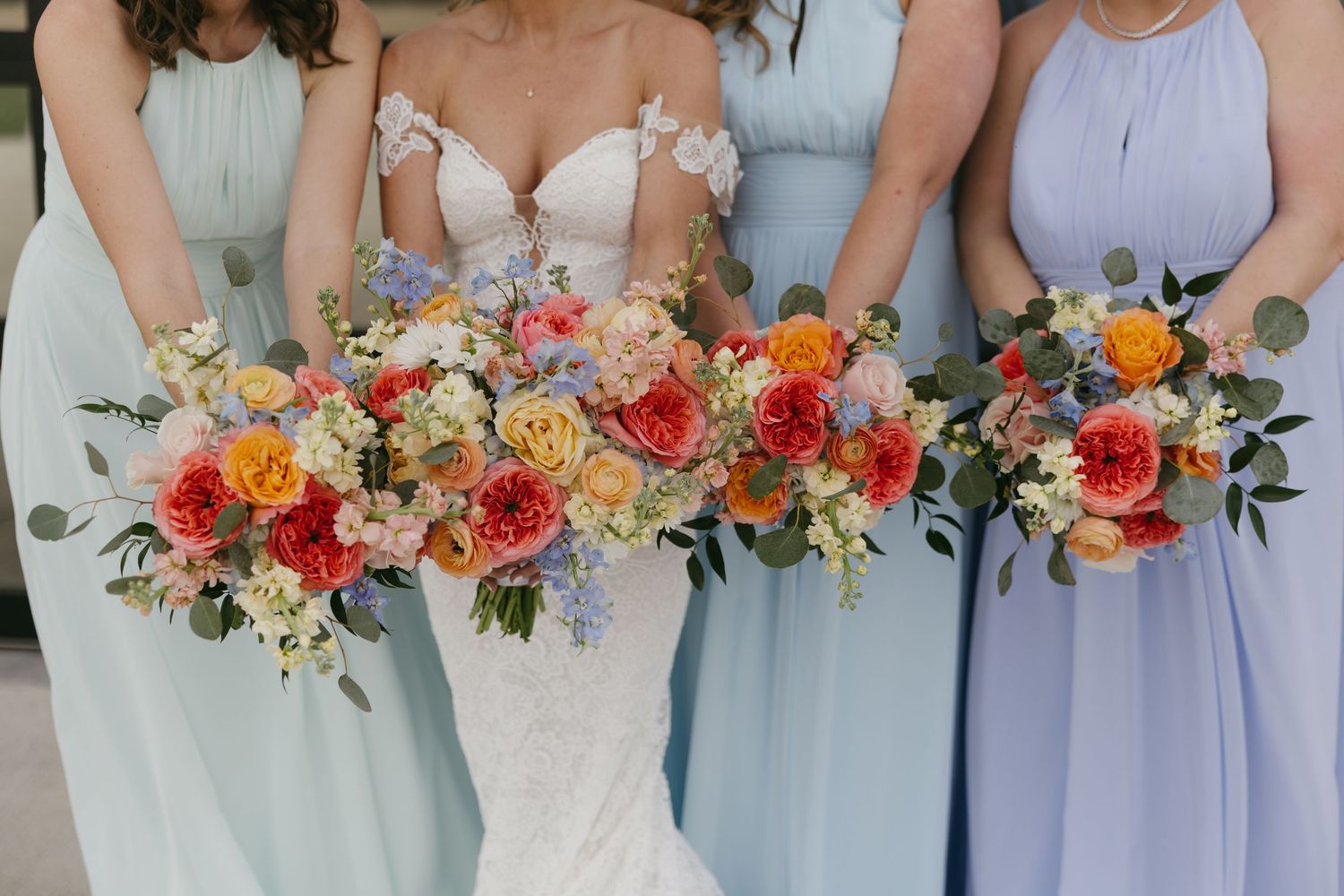 Bride and bridesmaids in blue gowns holding vibrant colorful bouquets of orange, yellow, and pink blooms.