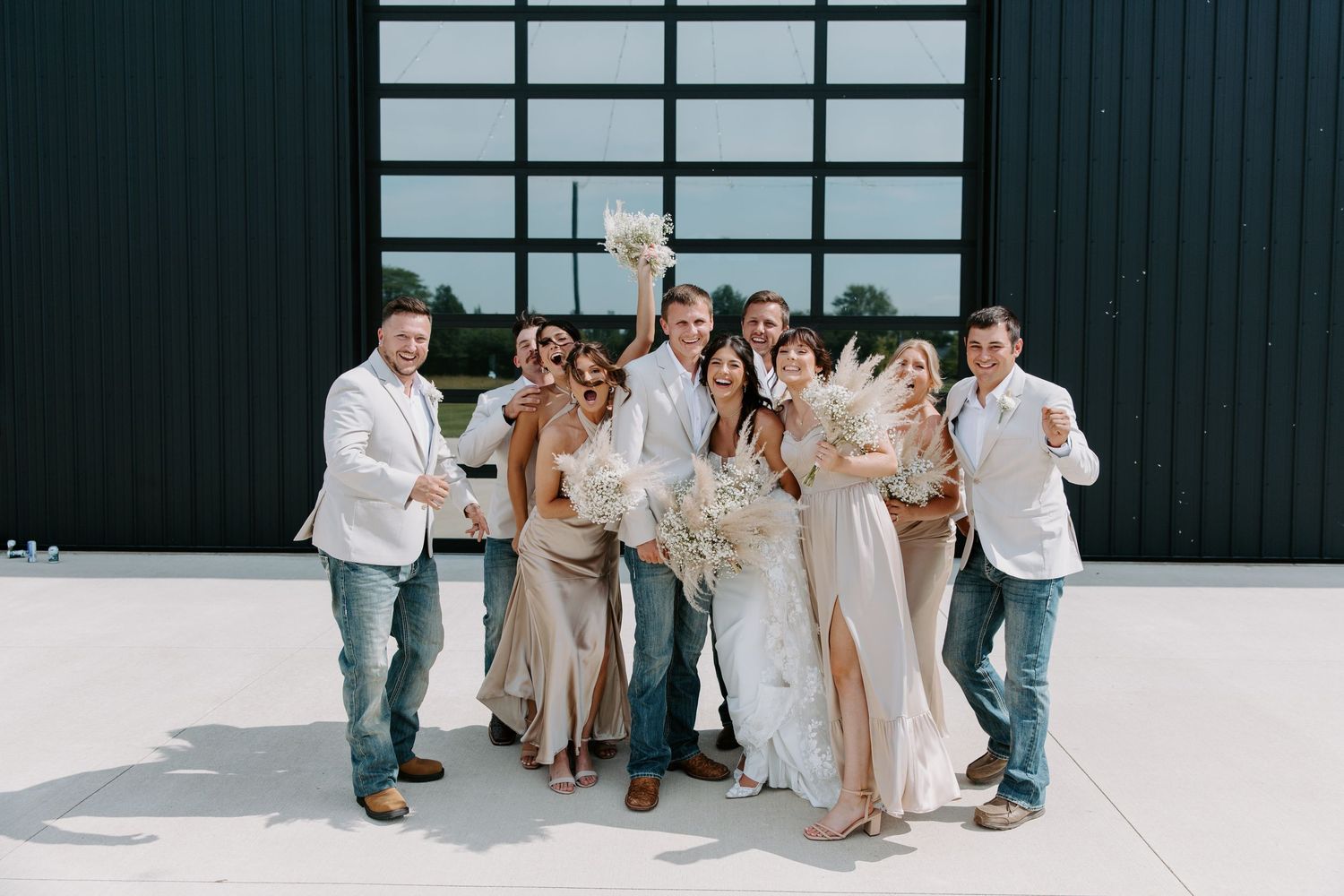 Wedding party celebrates together in front of a black barn, bride holding a boho white bouquet.