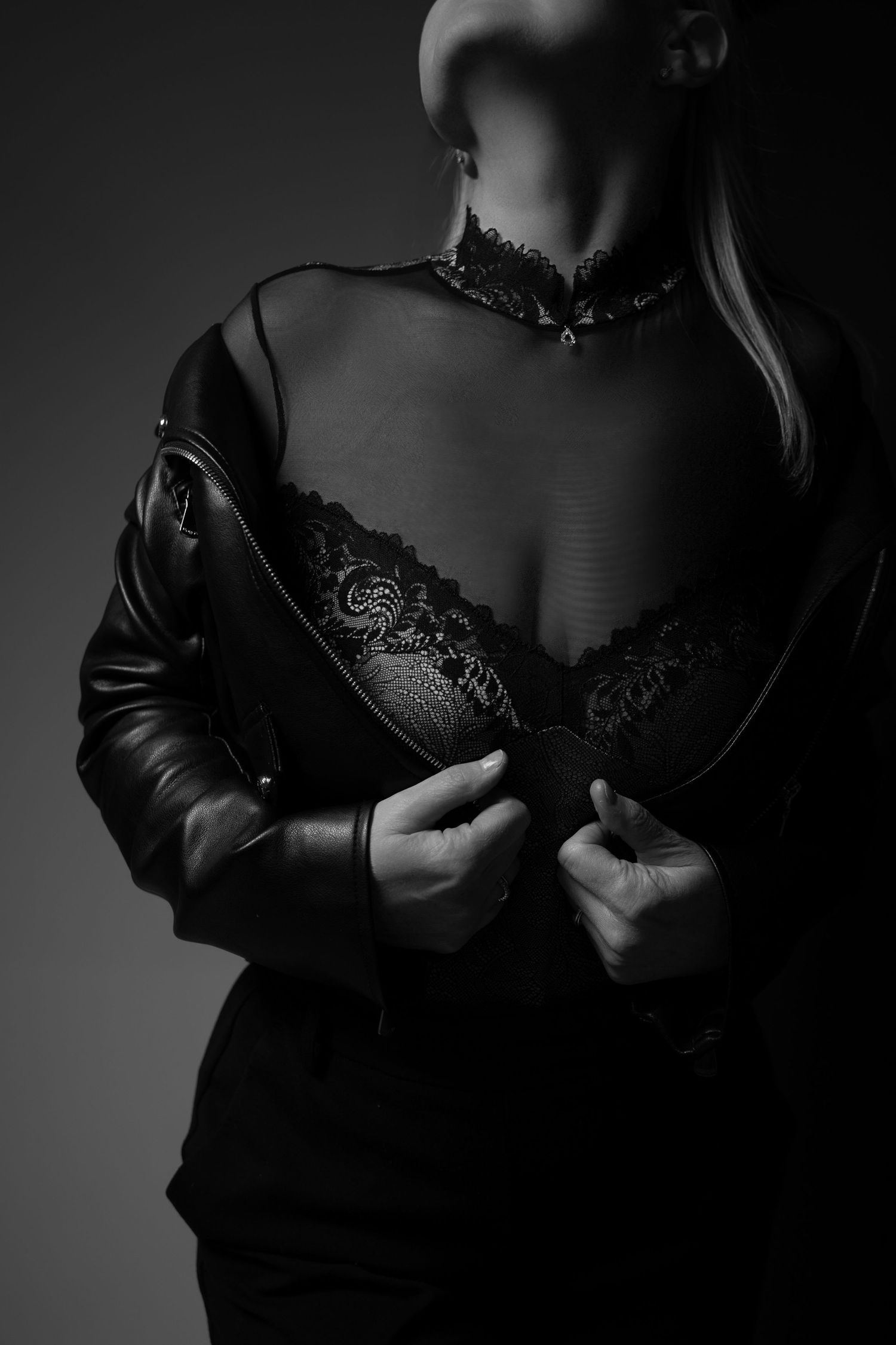 Black and white image of a woman in lace bra and mesh top holding open a leather jacket.