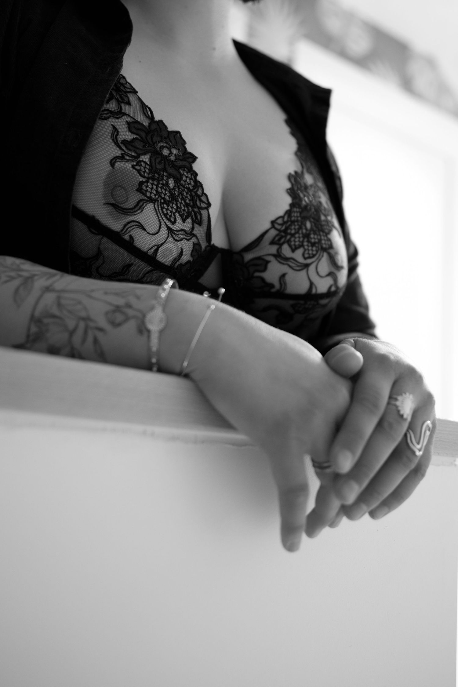 Close-up black and white photo of tattooed arms and lace bra resting on white surface.