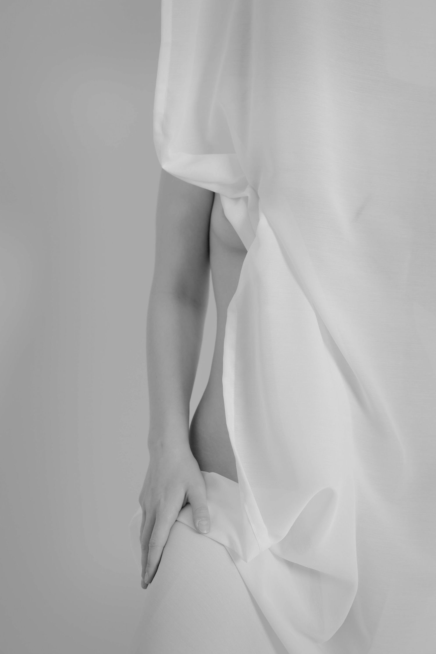 Black and white minimalist photo of a woman's arm emerging through flowing white sheer fabric.