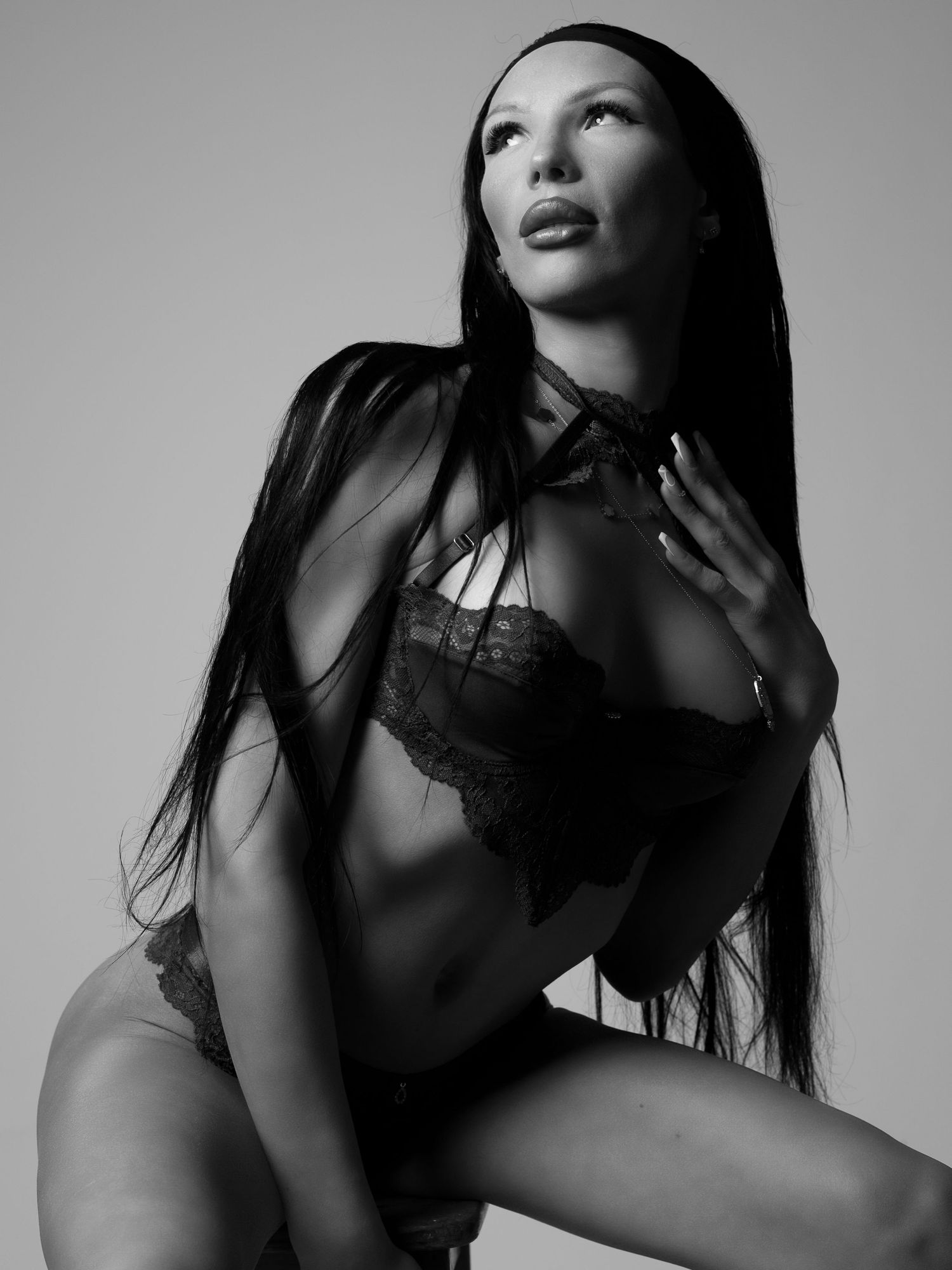 Black and white studio portrait of woman in lace lingerie with long dark hair looking upward.