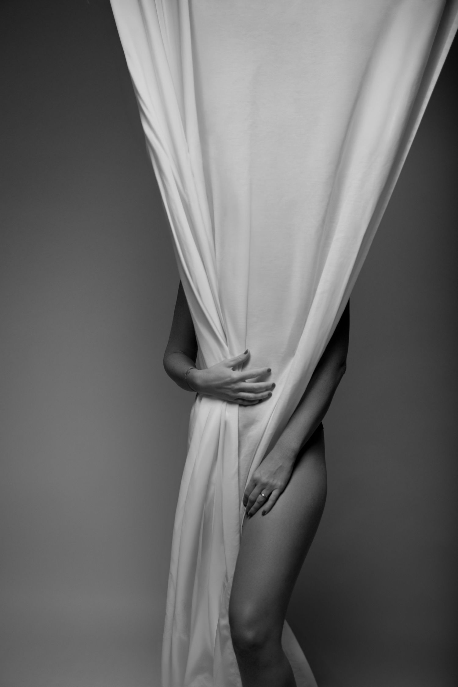 Black and white fine art photo of a woman draped in flowing white fabric, elegantly posed in a studio setting.