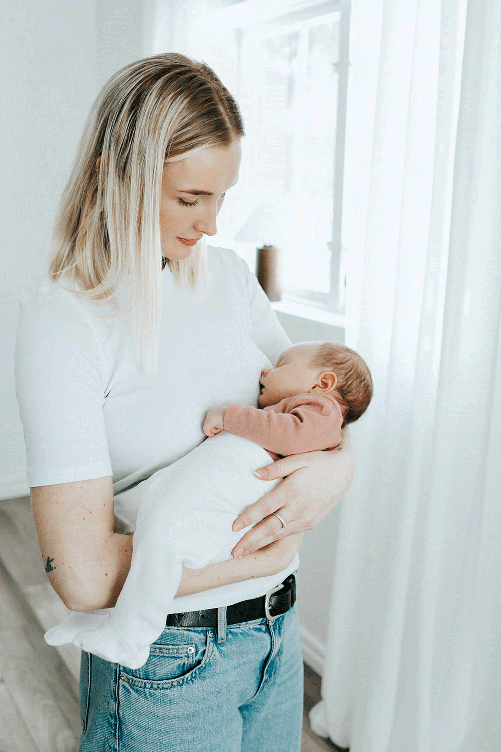 Ljus bild på mamma med sin bebis. Hon tittar ner mot bebisen som sover.