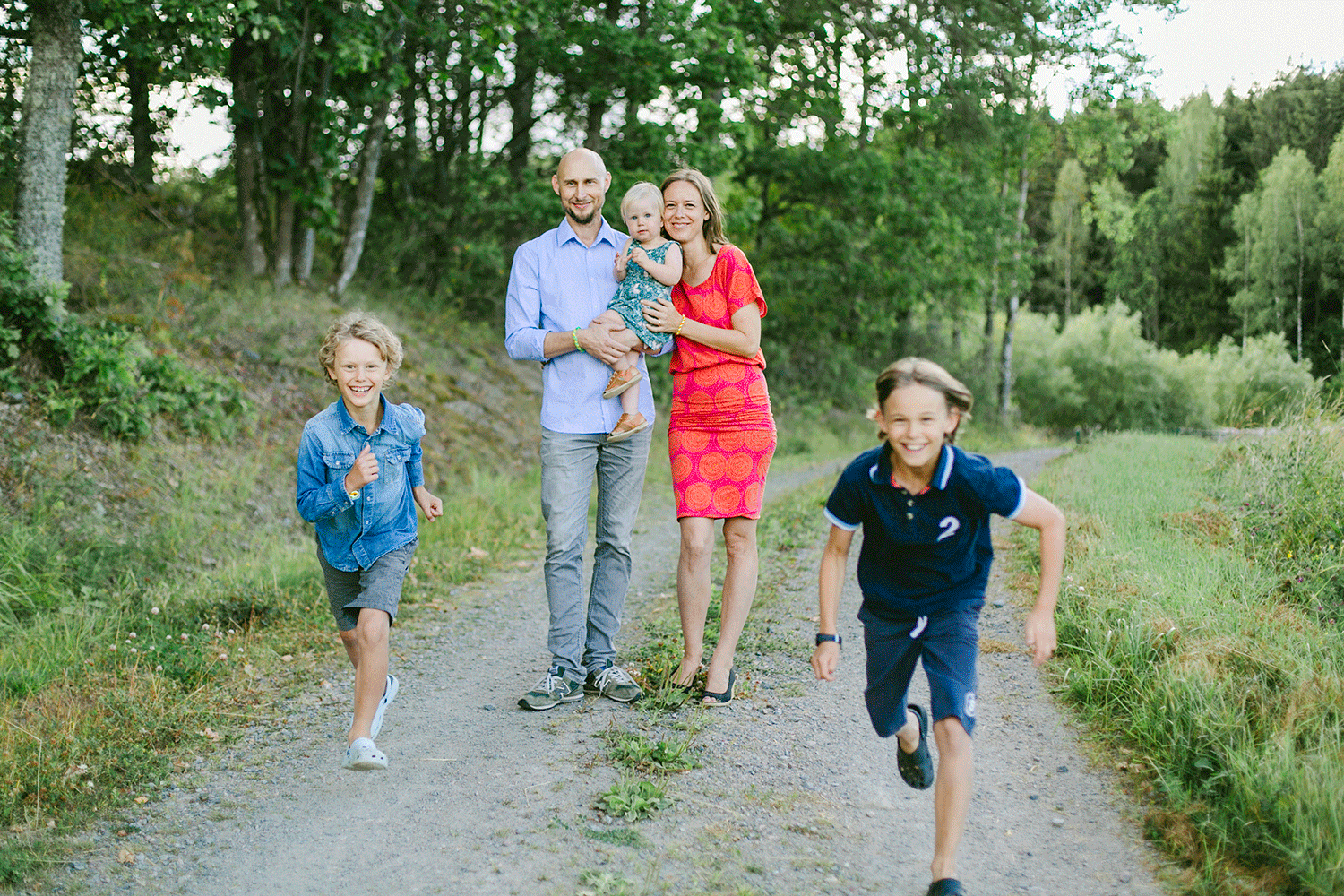 Familjefotografering i Sankt Anna. Mamma och pappa håller i bebis medan de två tonåringarna springer mot kameran.