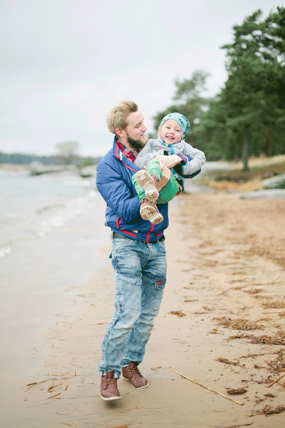 pappa som leker med sin son på stranden på Skutberget. Han lyfter upp honom och barnet skrattar.