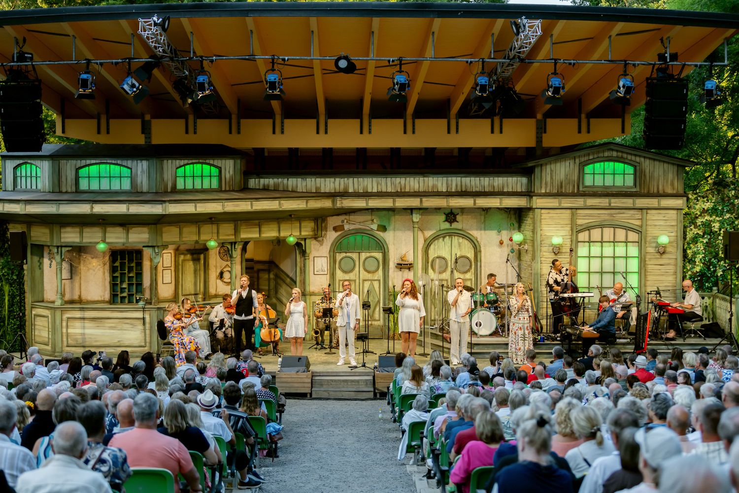 Musikalkväll med Peter Johansson. Emmi Christensson. Överblicksbild över scenen på Vallarnas Friluftsteater med Peter, Emmi och kören.