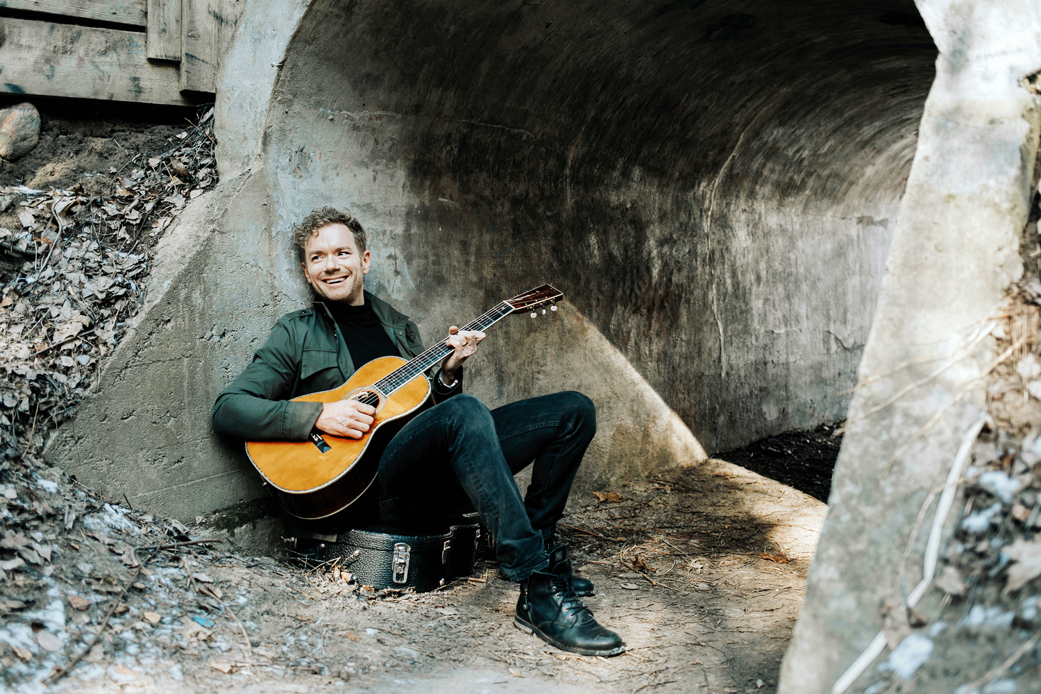 Peter Johansson som sitter i stenvalv på sitt gitarrfodral med gitarren i handen.