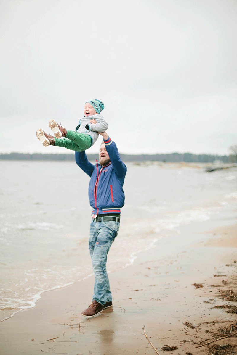 Pappa som står på en strand och kastar upp sitt barn i luften. barnet skrattar.