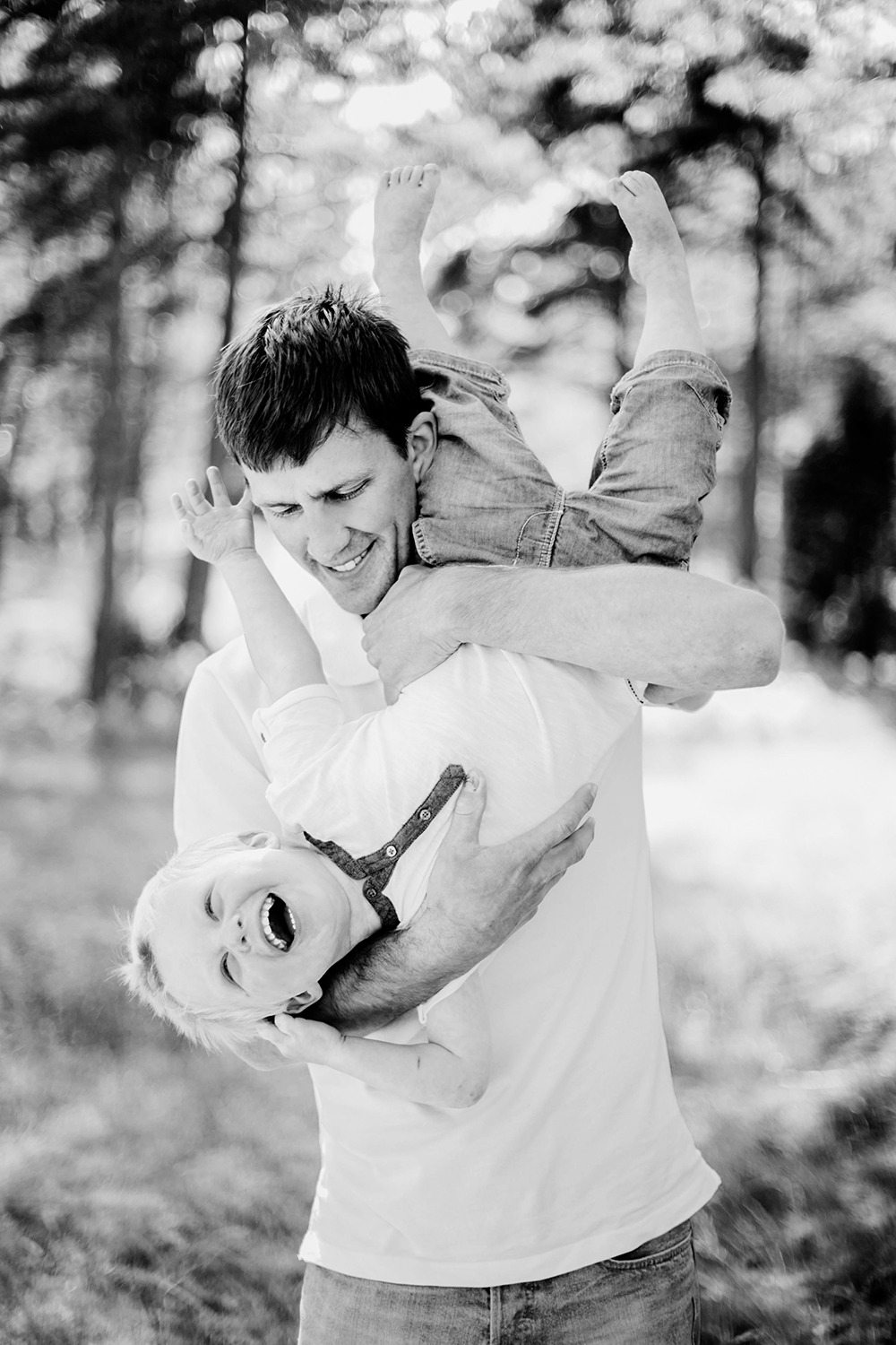 Pappa som leker med sin son genom att hålla honom upp och ner. svartvit.