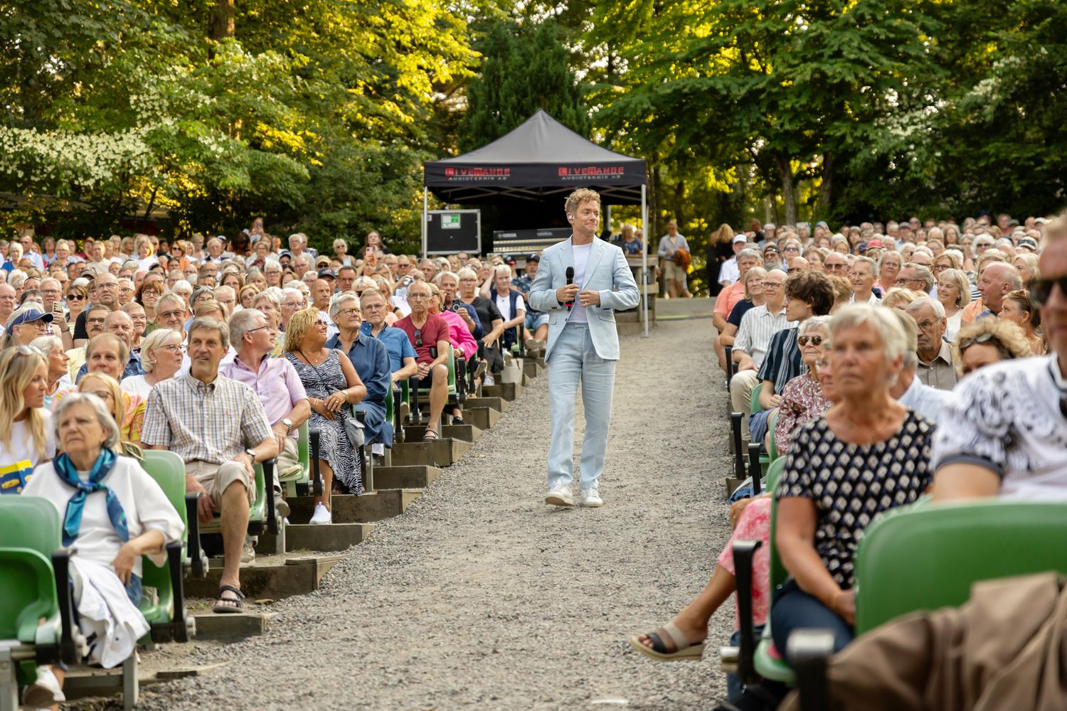 Musikalkväll med Peter Johansson o Emmi Christensson. Peter bland publiken på Vallarnas Friluftsteater. han går i grusgången.