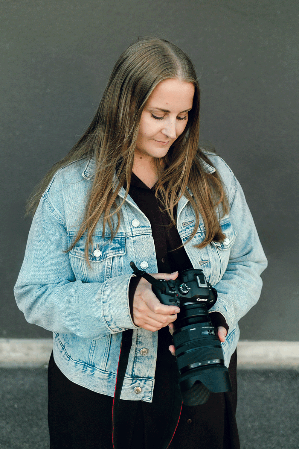 Porträtt på mig, fotograf Rebecca Nordin. Jeansjacka på mig och håller i kameran. Tittar ner.