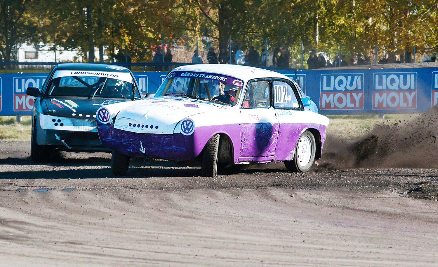 Två Folkracebilar. Den lila bilen sladdar framför den blå bilen.