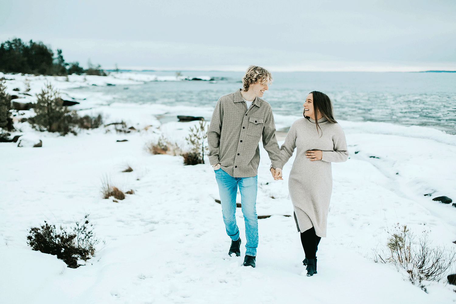 Gravid kvinna som går hand i hand med sin man i snön. Bakom dem är en frusen sjö.