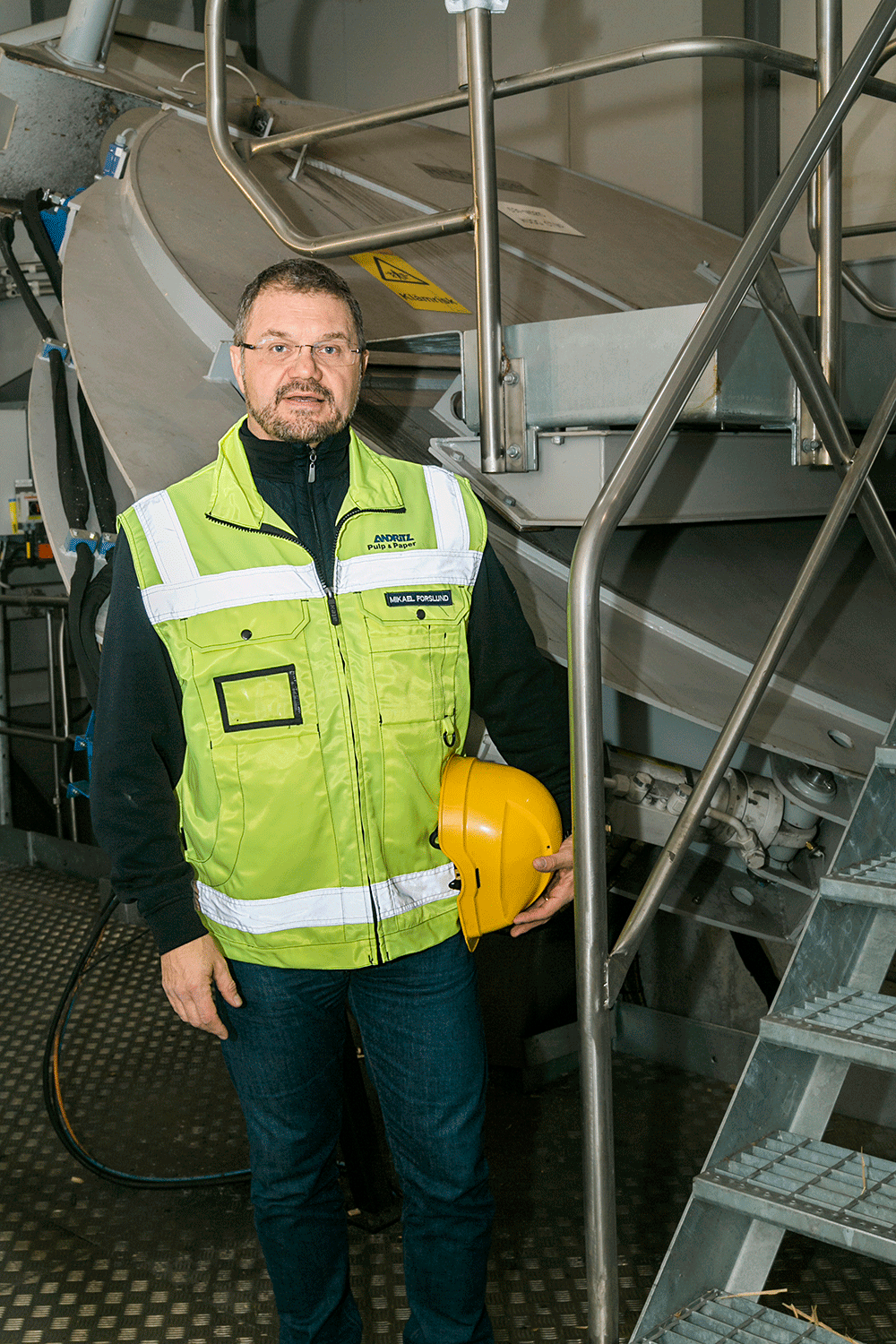 Mikael Forslund på Andritz posar med hjälm och reflexväst framför maskin på fabriken.