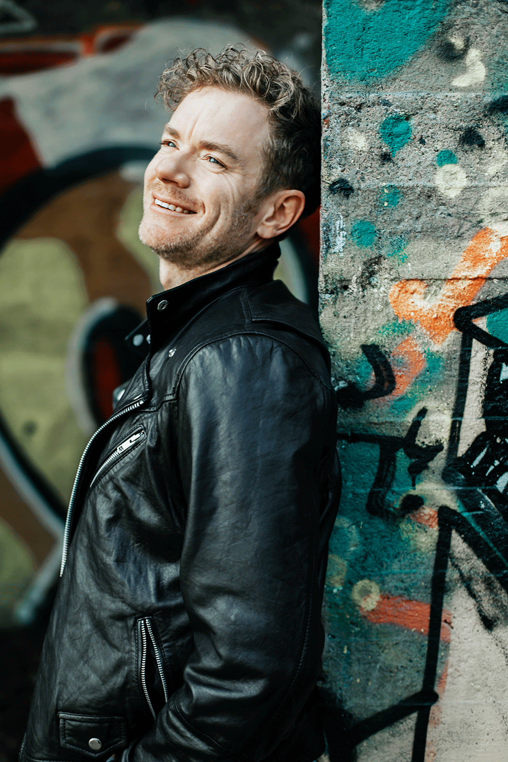 Pressbild på Peter Johansson. Han har skinnjacka och tittar uppåt. Grafitti på väggarna.