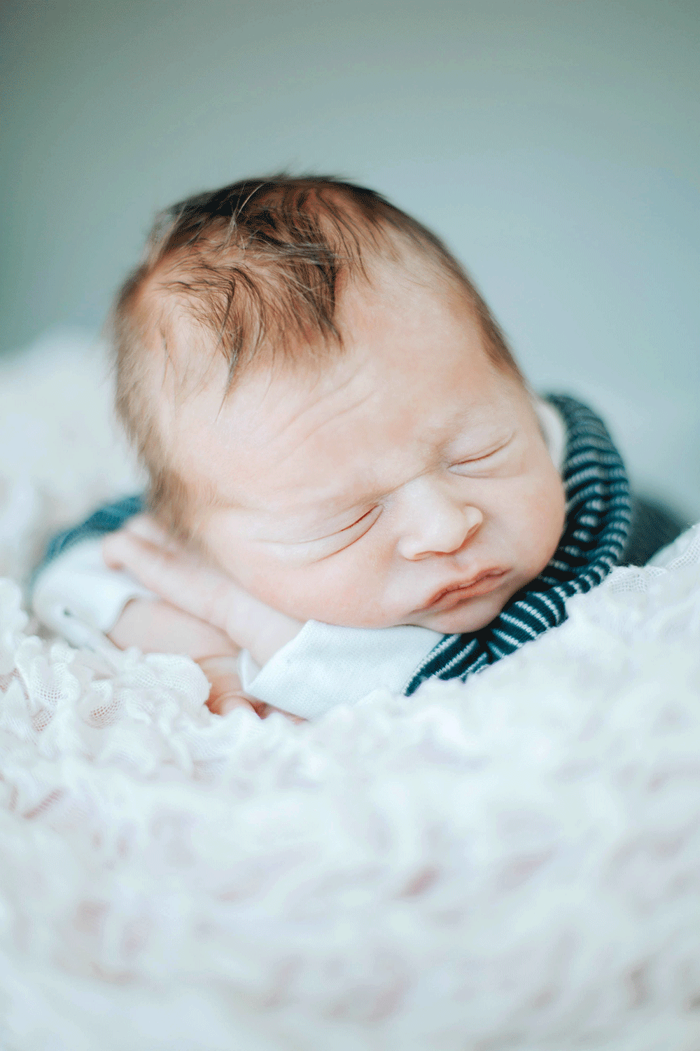 Nyfödd bebis ligger och sover på sina armar på en filt.