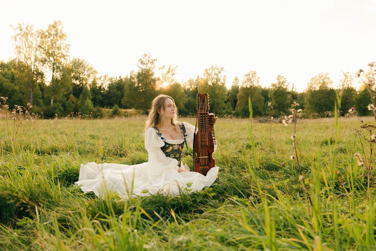 Porträtt på Julia Johansson i Karlstad. Julia sitter på ängen tillsammans med sin nyckelharpa. Headshot.