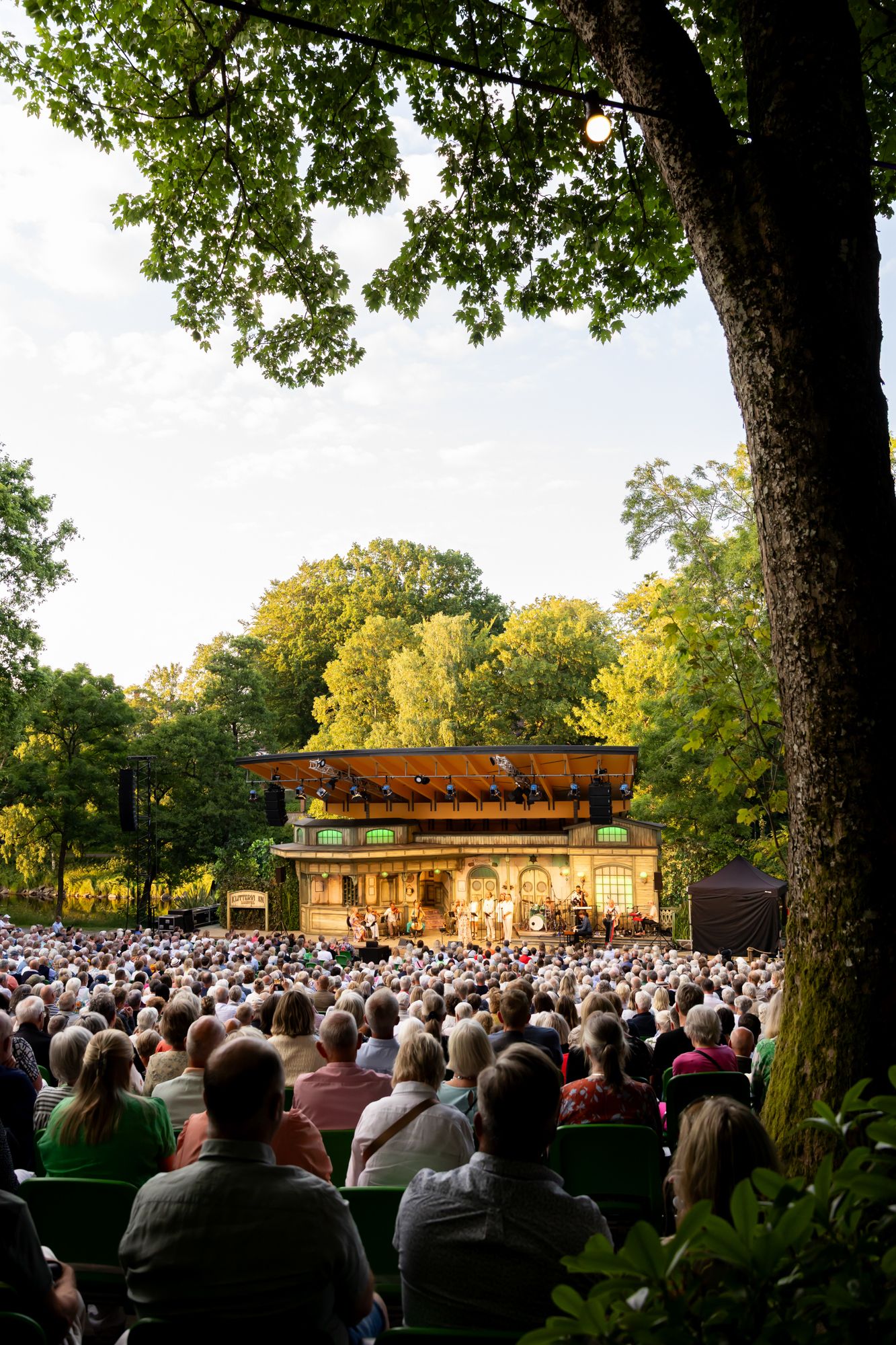 Musikalkväll med Peter Johansson o Emmi Christensson. Överblicksbild över scenen på Vallarnas Friluftsteater med träd i förgrund.